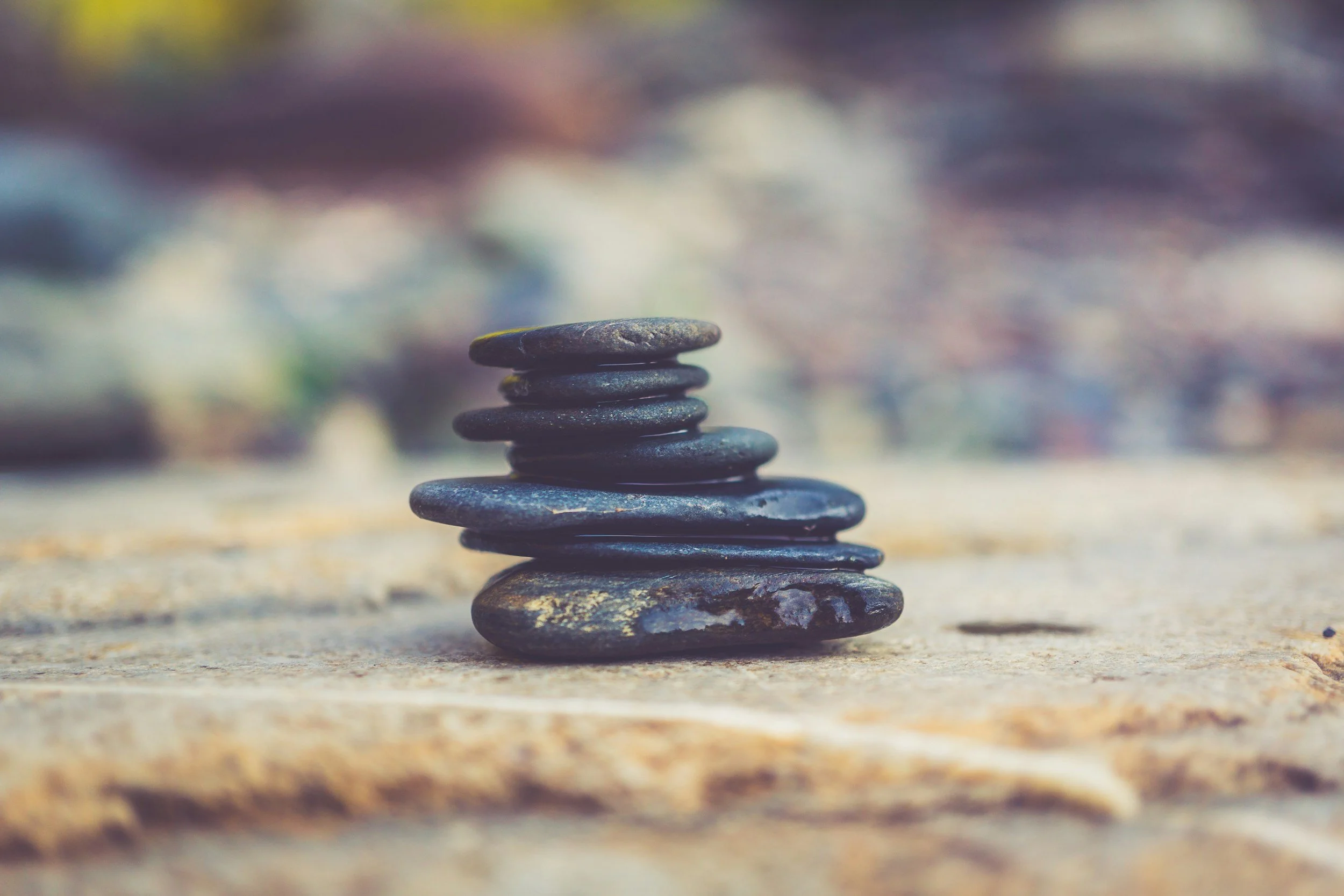 Stacked black stones on a sandy surface with a blurred background.