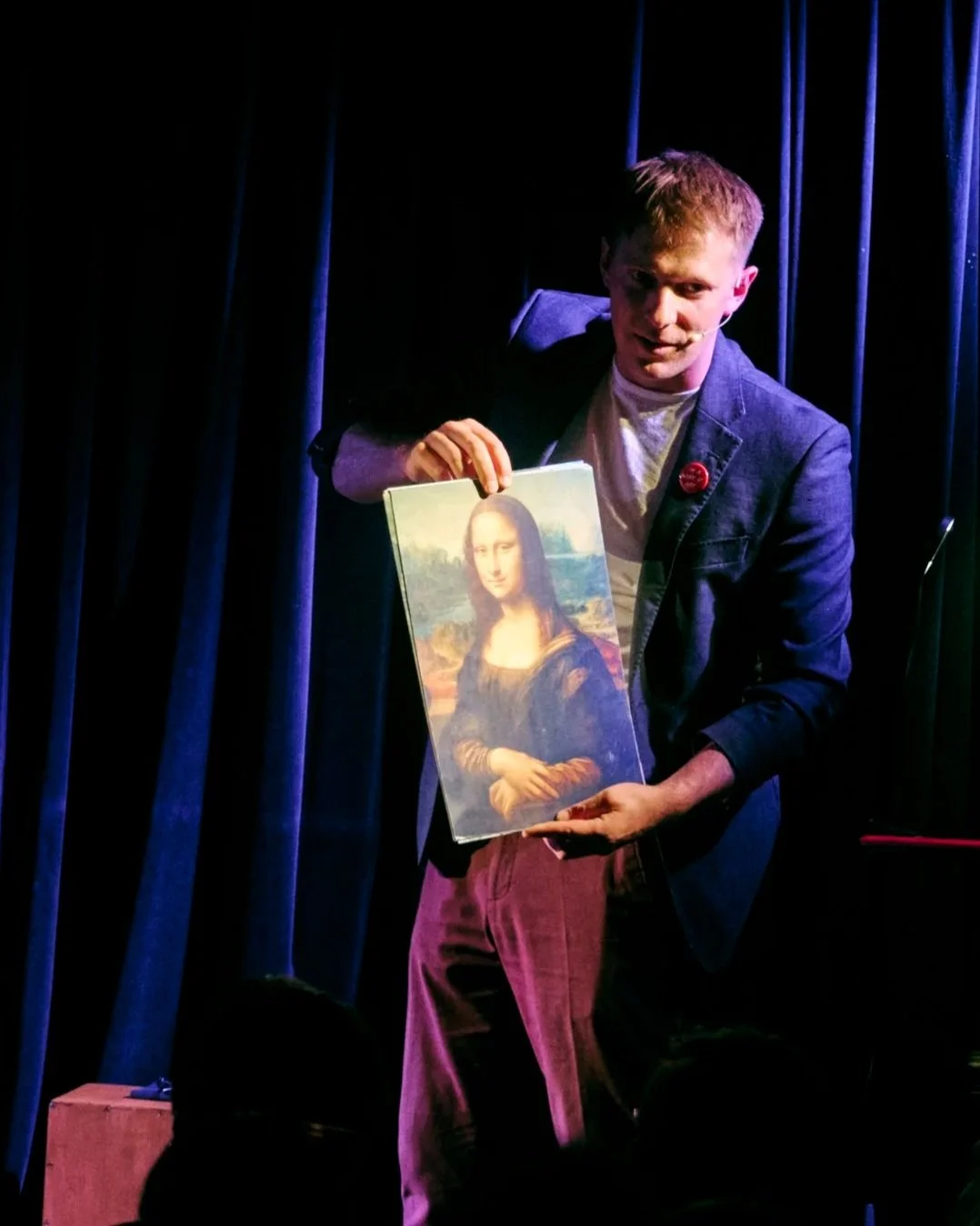 A man on a stage holding a picture of the Mona Lisa painting.