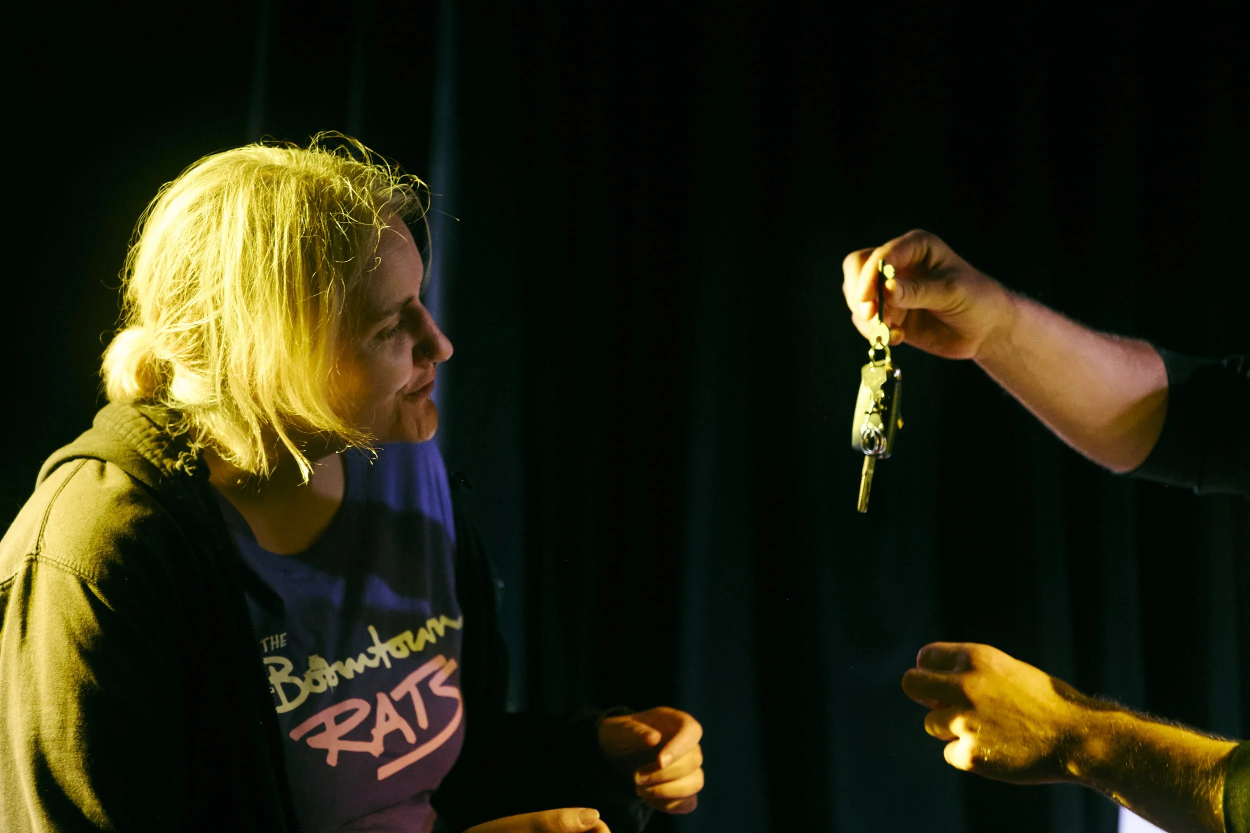 A woman with blonde hair looking at a set of keys being handed to her by an unseen person.