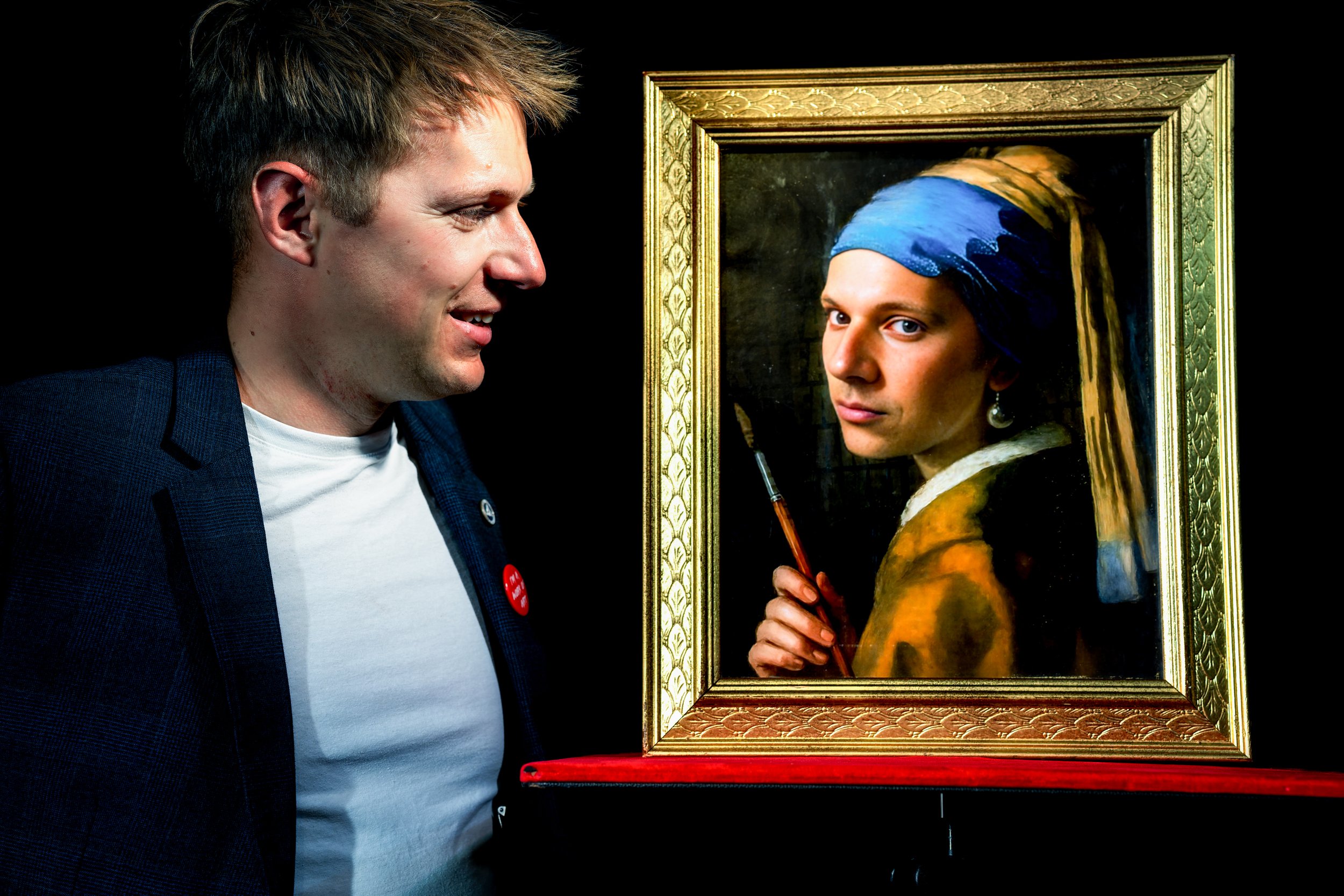 A man in a dark blazer and white shirt looking at Leonardo da Vinci's Mona Lisa painting with a smile.