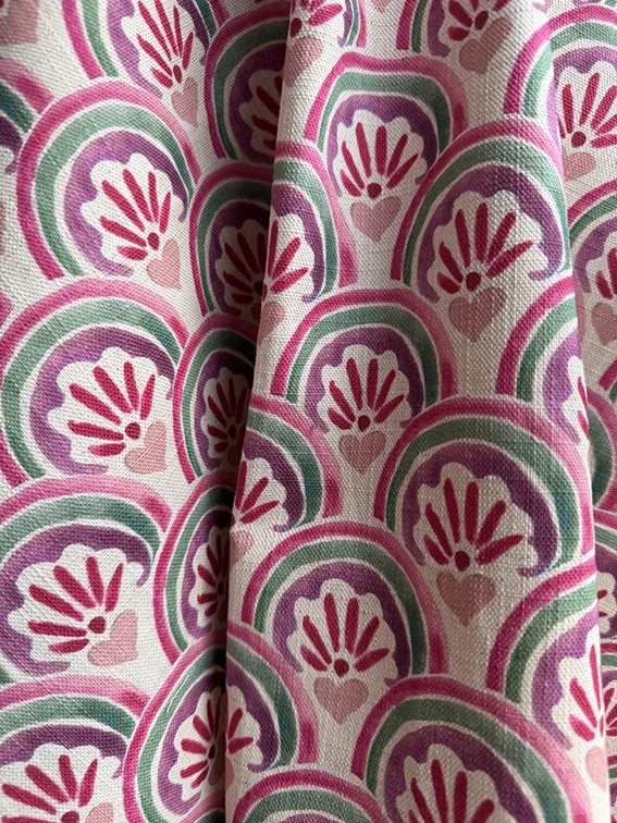 Close-up of fabric with a repeating colorful rainbow pattern featuring hearts in pink, purple, and green hues.
