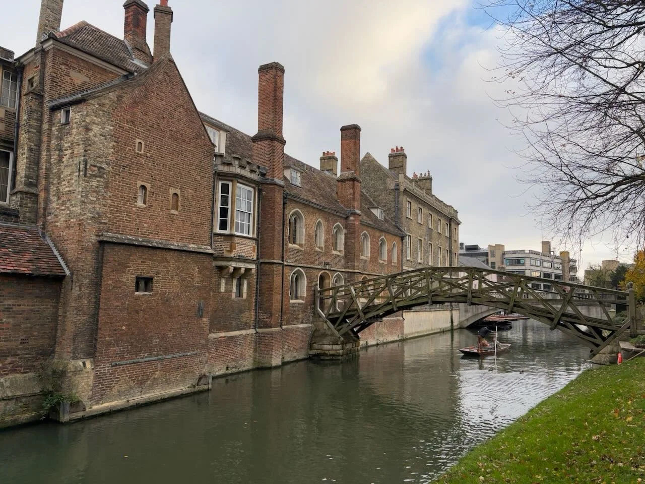 Historic brick buildings along a canal with a small wooden footbridge and people boating.
