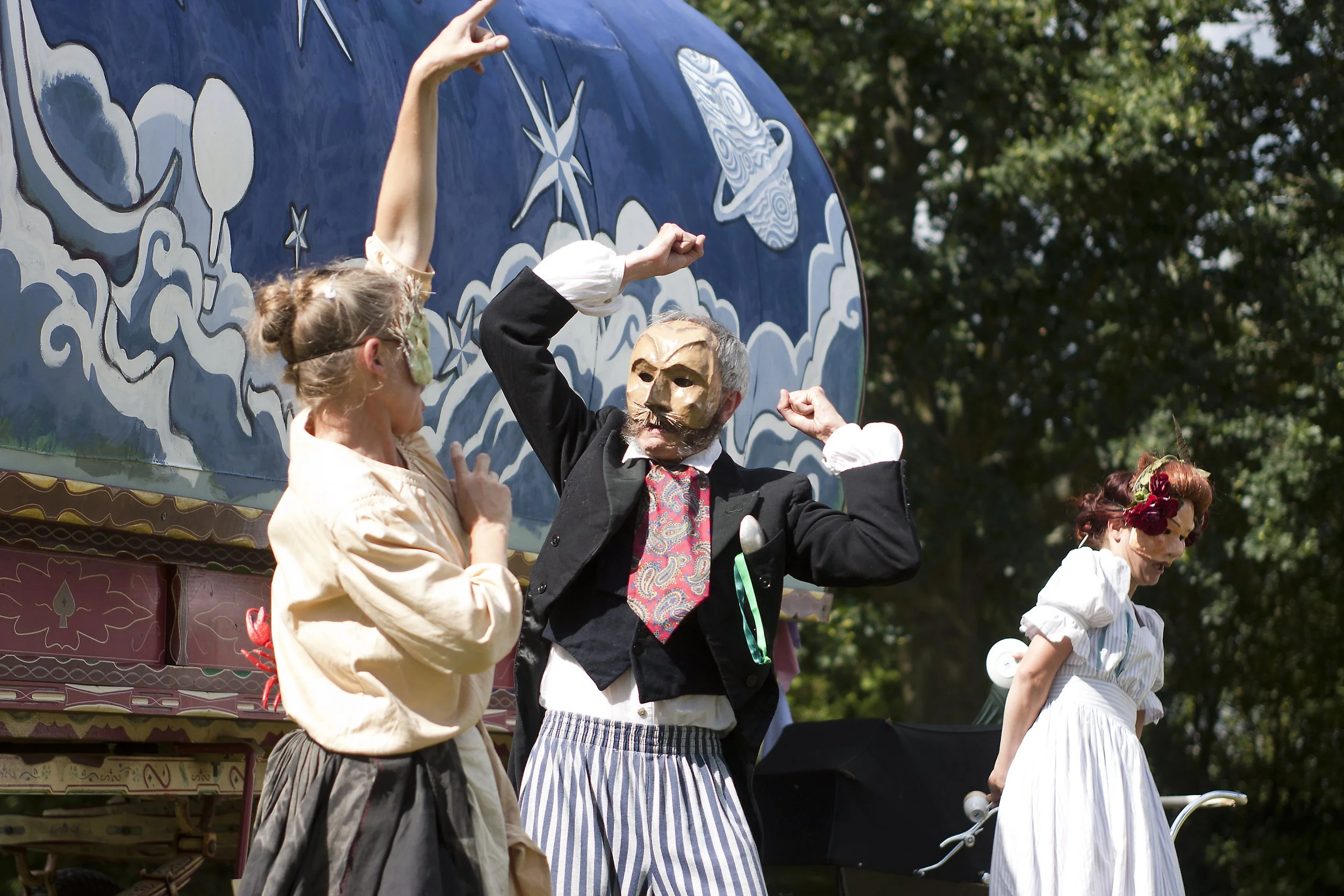 People in vintage costumes performing on a stage decorated with cloud and star motifs outdoors, with trees in the background.