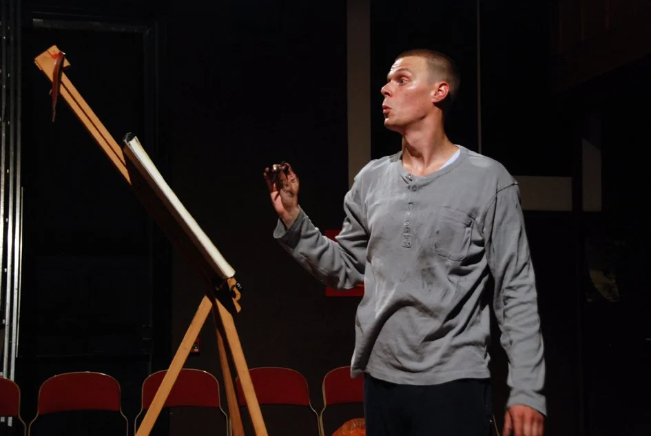 A man standing next to an artist's drawing board, holding a marker, looking intently at the drawing.