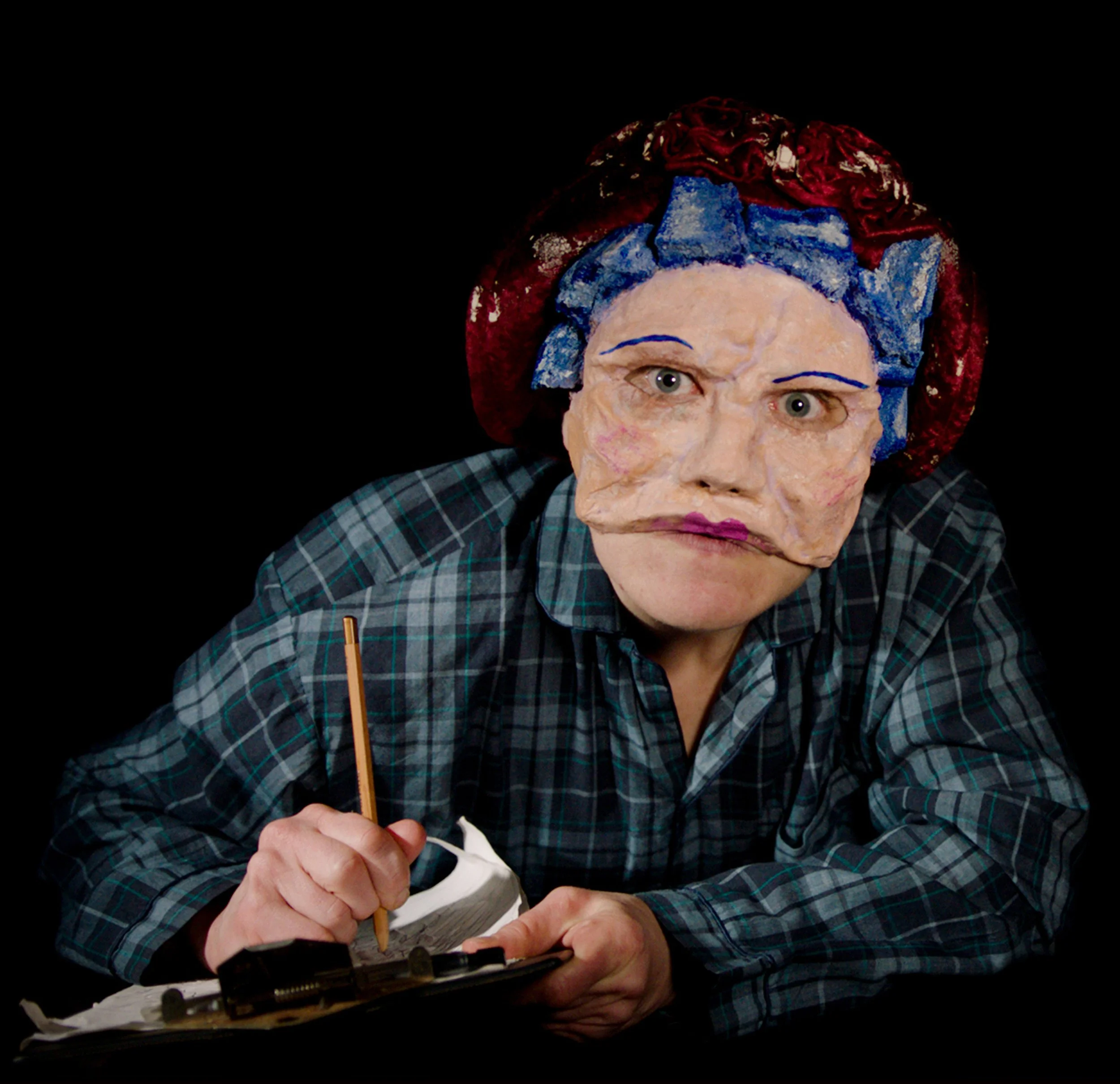 Close-up of a person applying makeup or face paint, holding a brush and a sponge, wearing a plaid shirt, with a partial view of the person's face and hand, against a black background.