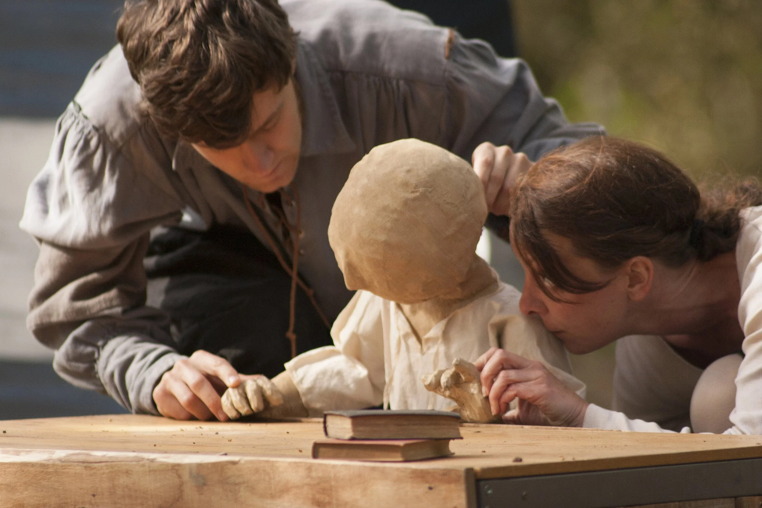 Two individuals examining a skeletal model made of white material on a wooden table, with books nearby.