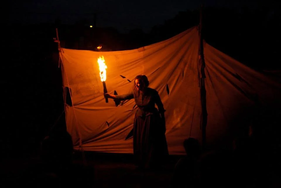 Performer holding a lit torch on a dark stage with a large fabric backdrop
