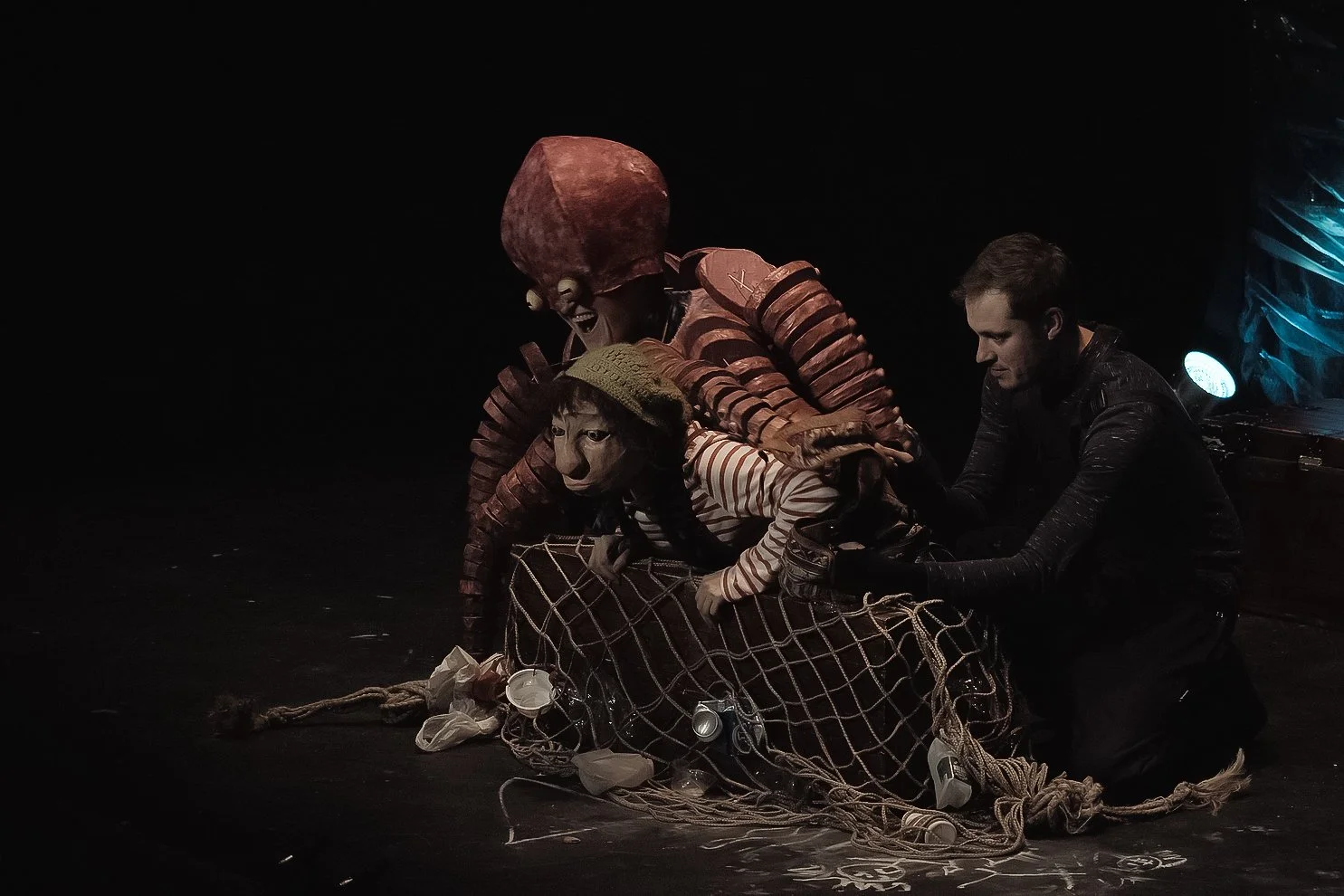 A stage performance featuring two actors in costumes, one dressed as an octopus, and a human with a lion mask, with theatrical lighting and props on stage.