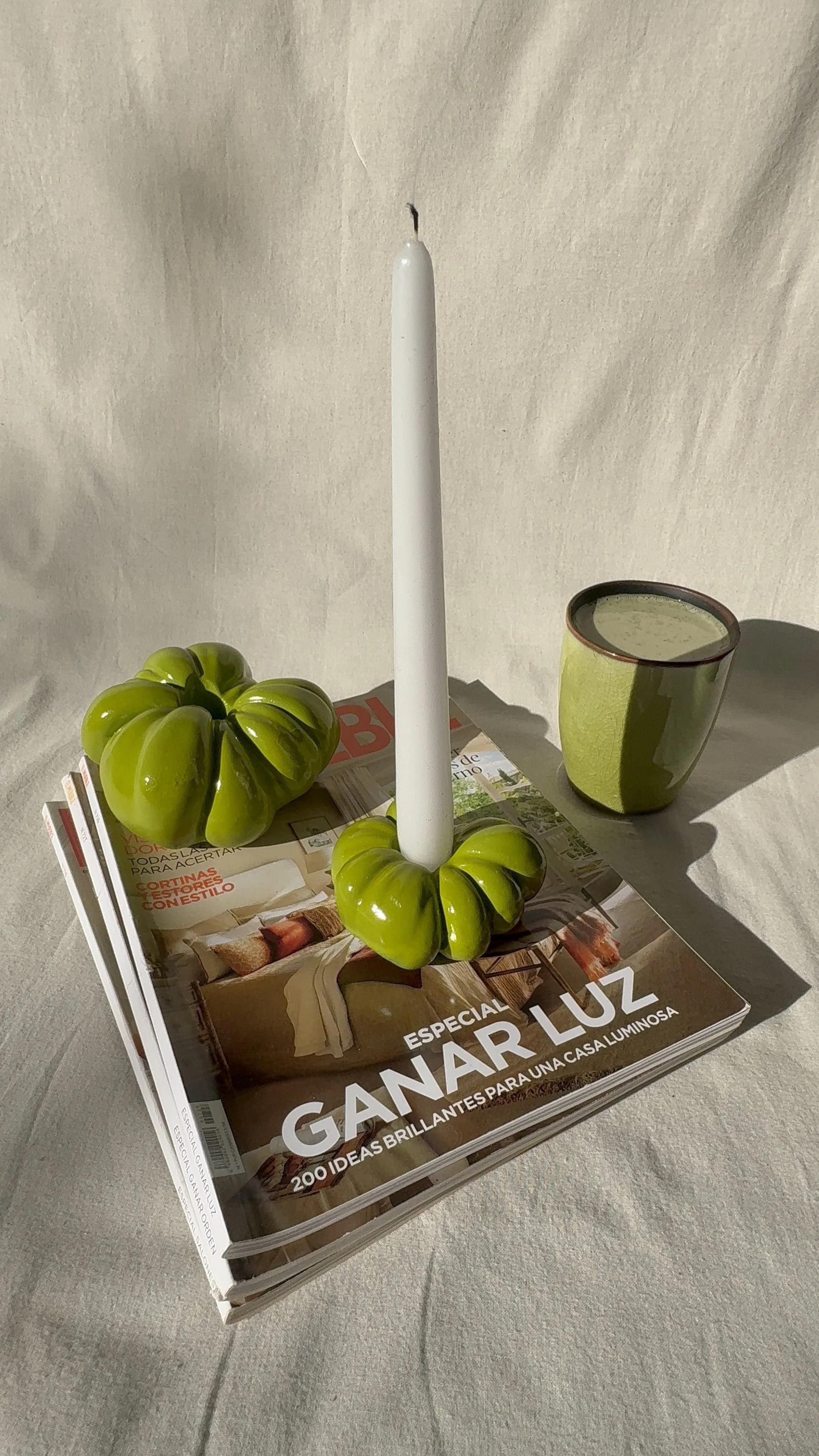 A table display with a stack of magazines, a green ceramic candle holder with a white candle, a green ceramic cup, and two green ceramic pumpkin-shaped objects.