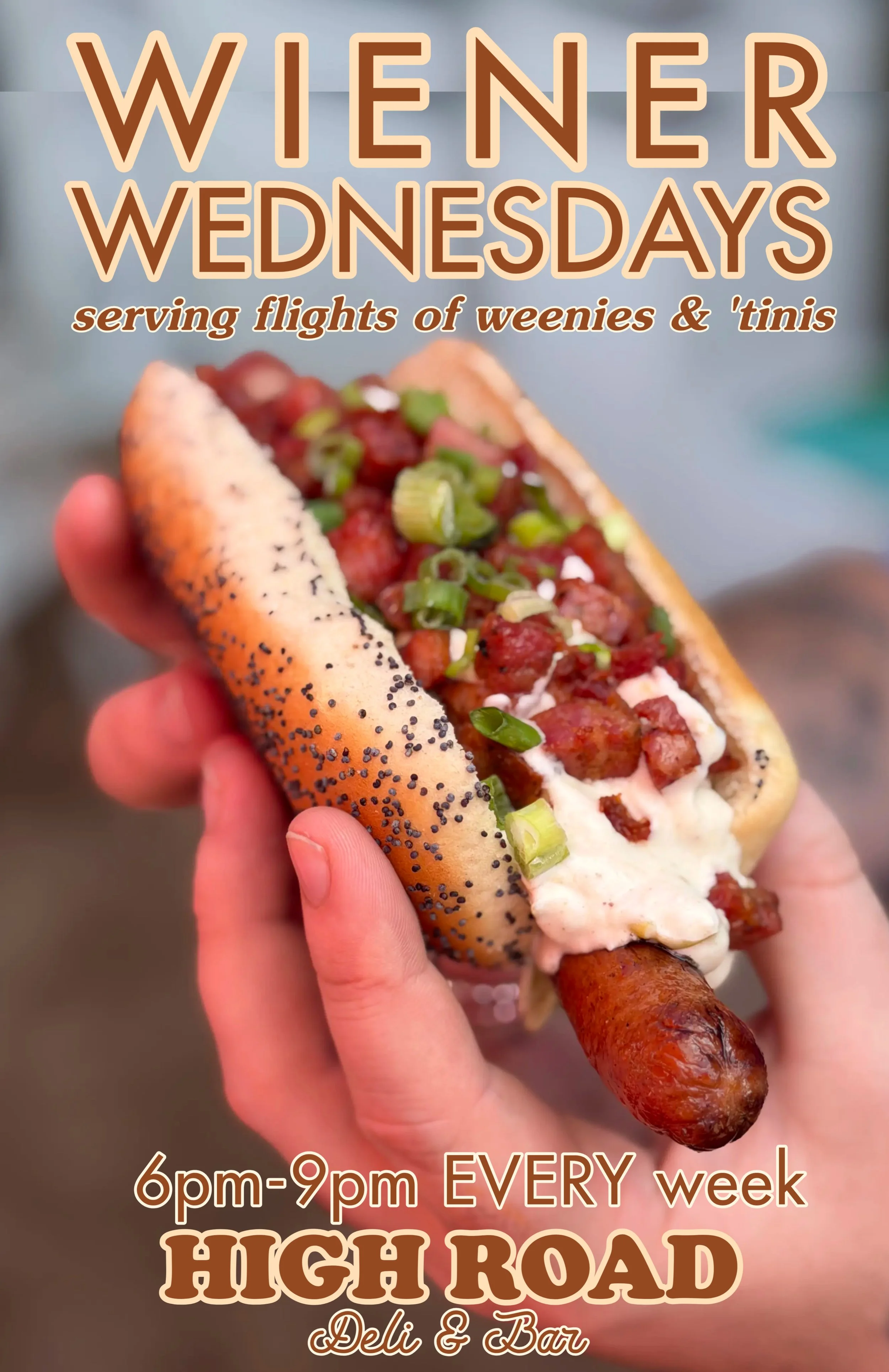 Hand holding a house made hot dog with toppings. Featuring flights of martini and flights of weenies on Wednesday nights at High Road Deli & Bar.