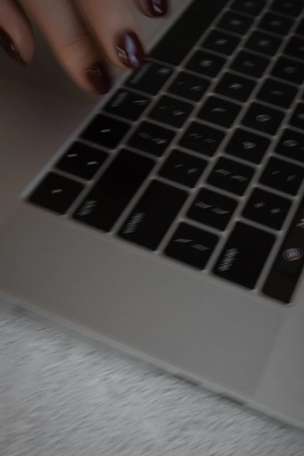 Close-up of a person's hand with dark painted nails typing on a laptop keyboard.