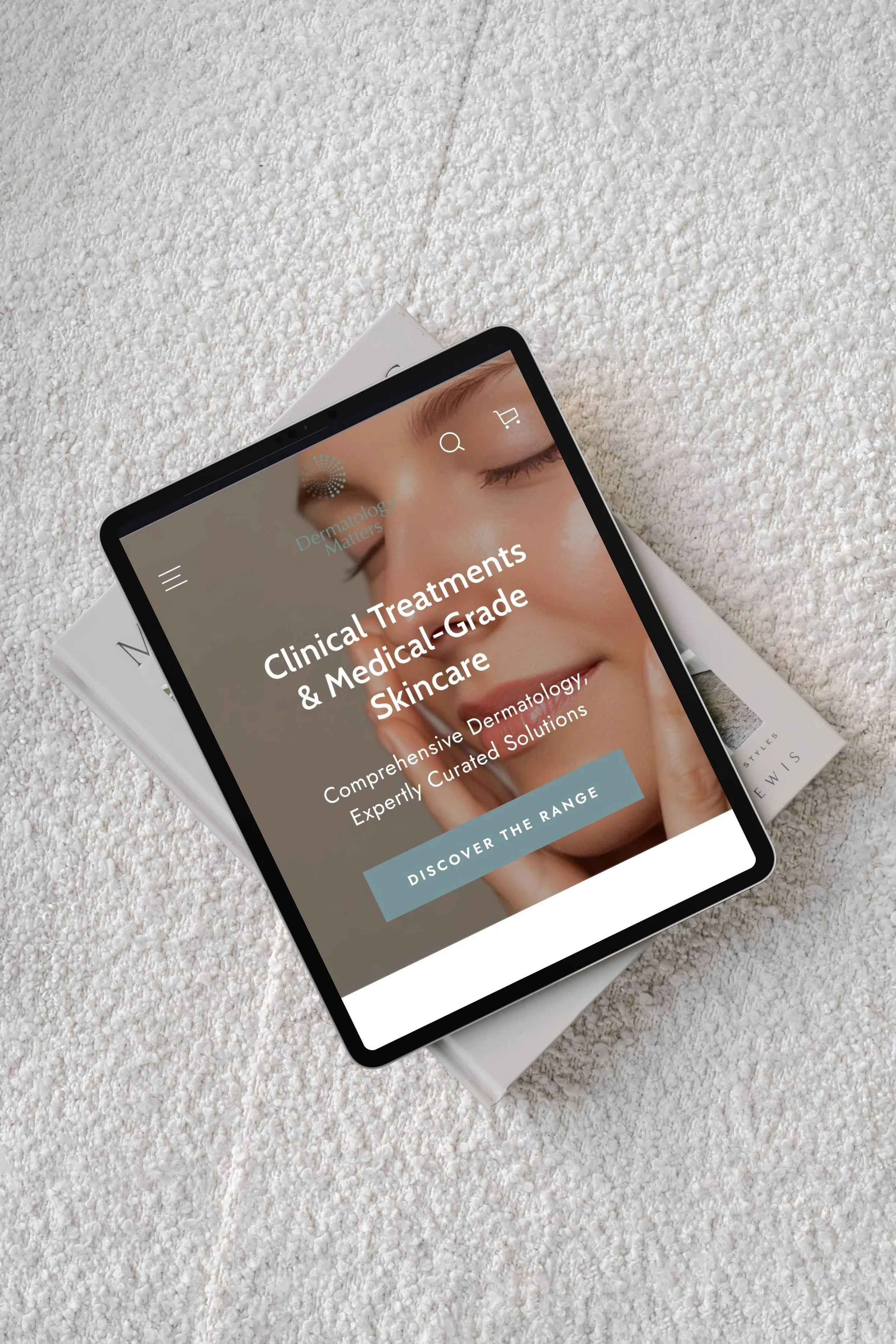 Tablet displaying a dermatology skincare website on a white textured surface with a magazine underneath.