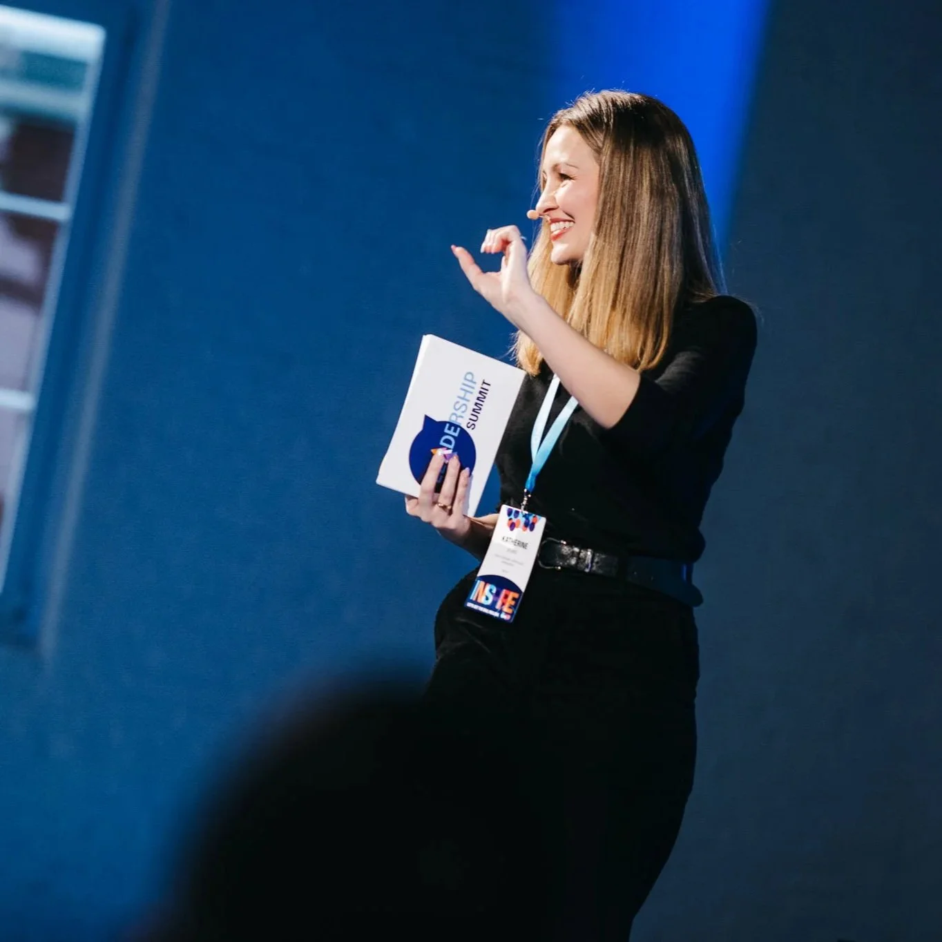 Woman speaking at a wellbeing and stress management conference, holding presentation materials and smiling