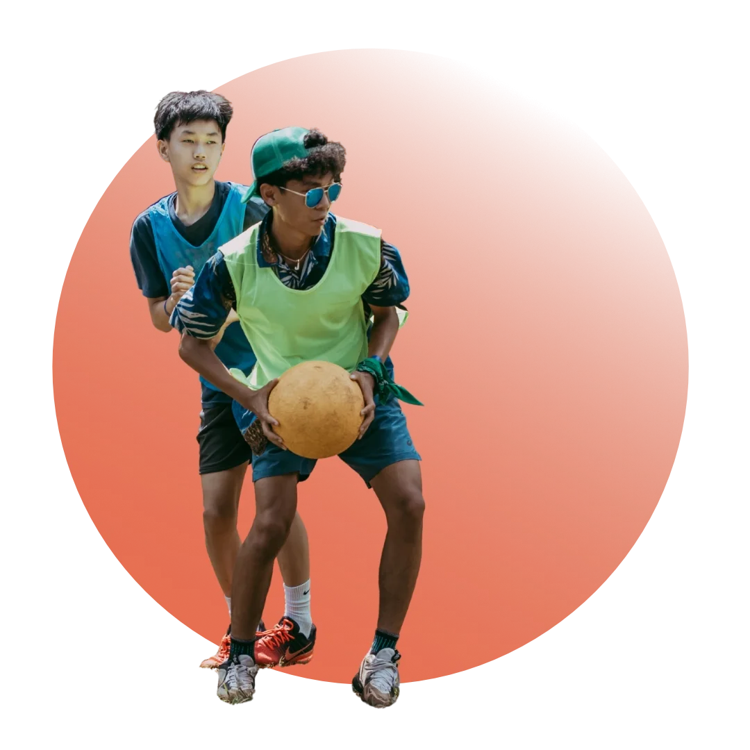 Two young men playing a game that involves holding a large round object, possibly a ball, against a bright orange background.