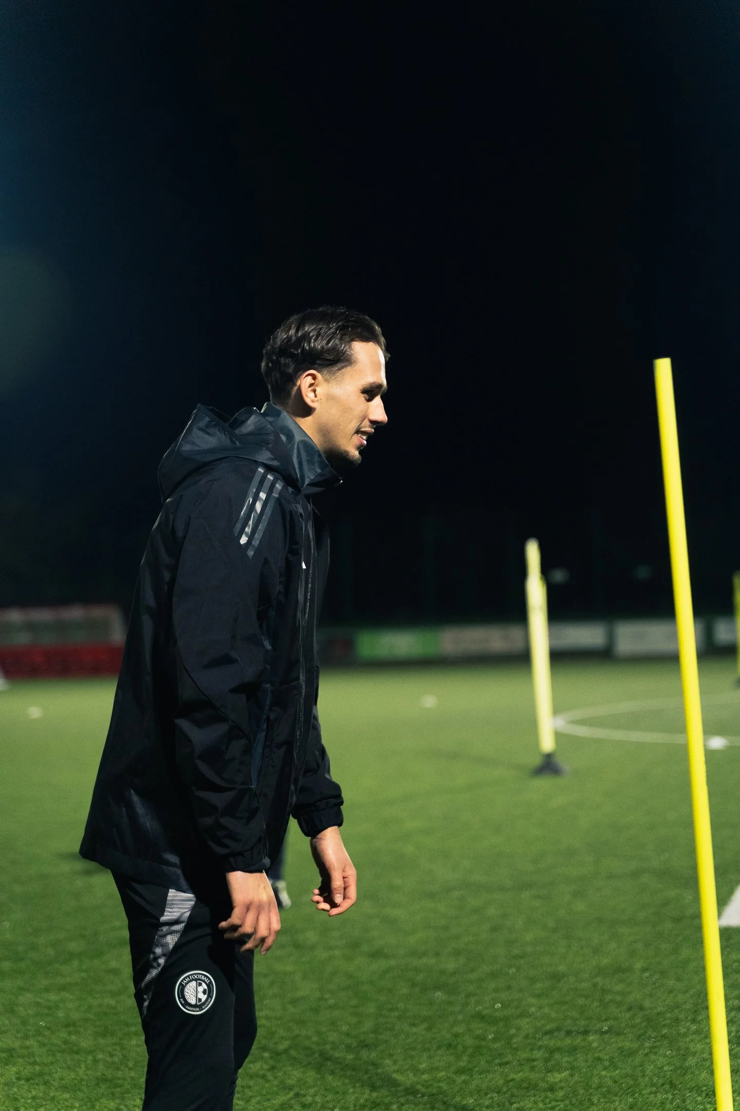 A man in training gear practicing football on a field at night.