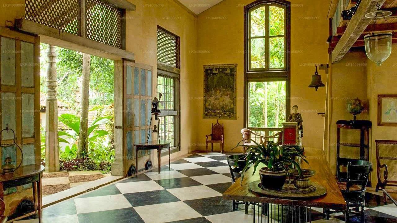Interior of a vintage-style room with large windows, checkered black and white floor, and eclectic furniture. Outside greenery is visible through open doors and windows.