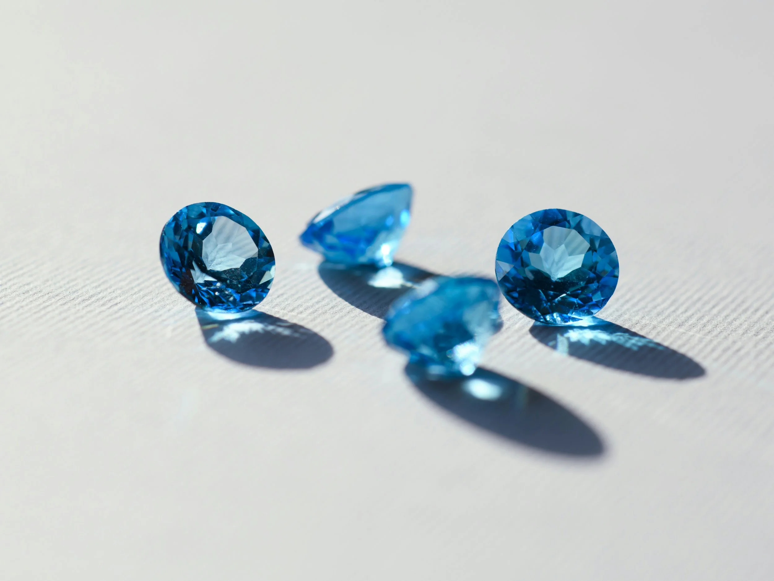 Three blue gemstones, two round and one pear-shaped, arranged on a white surface with shadows