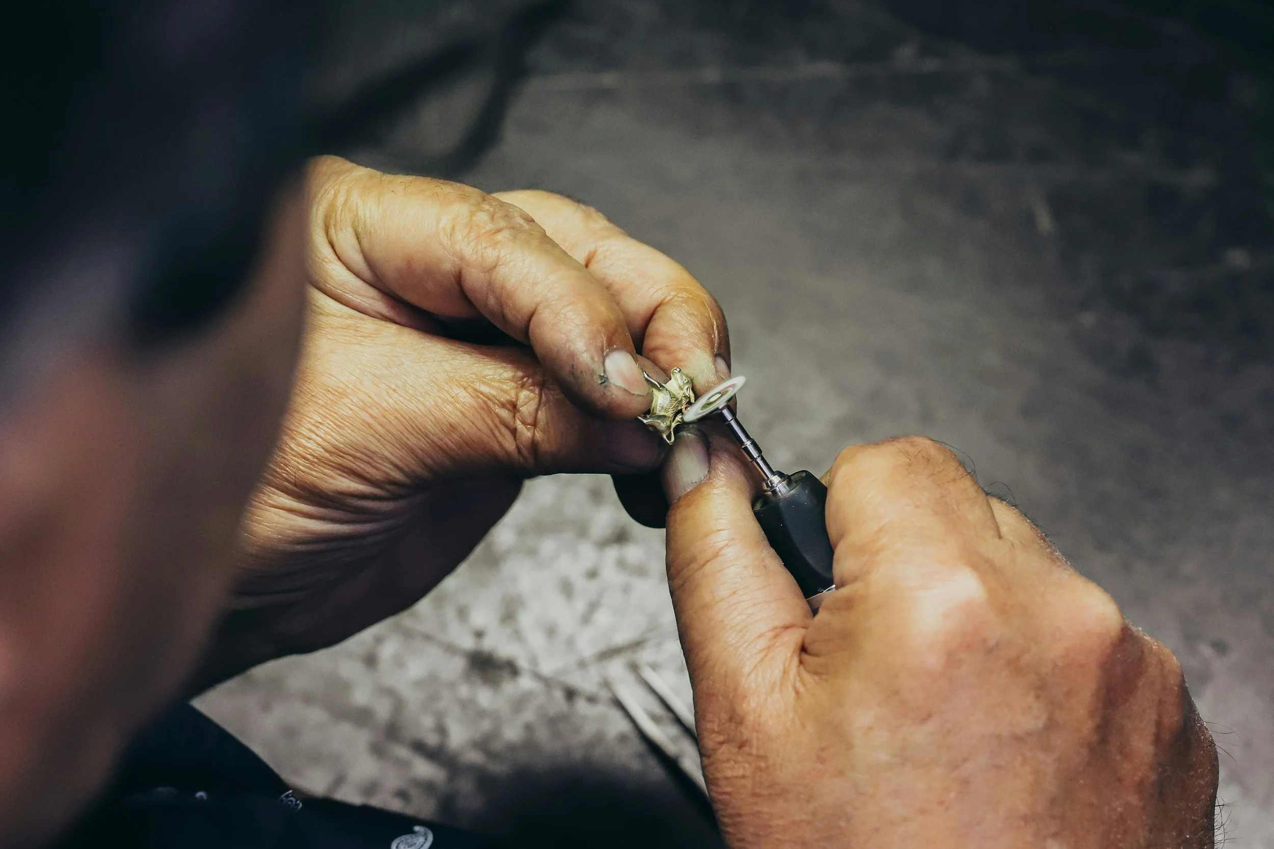 A person working with a rotary tool, polishing or grinding a small metallic object, possibly jewelry or small machine part, in a workshop setting.