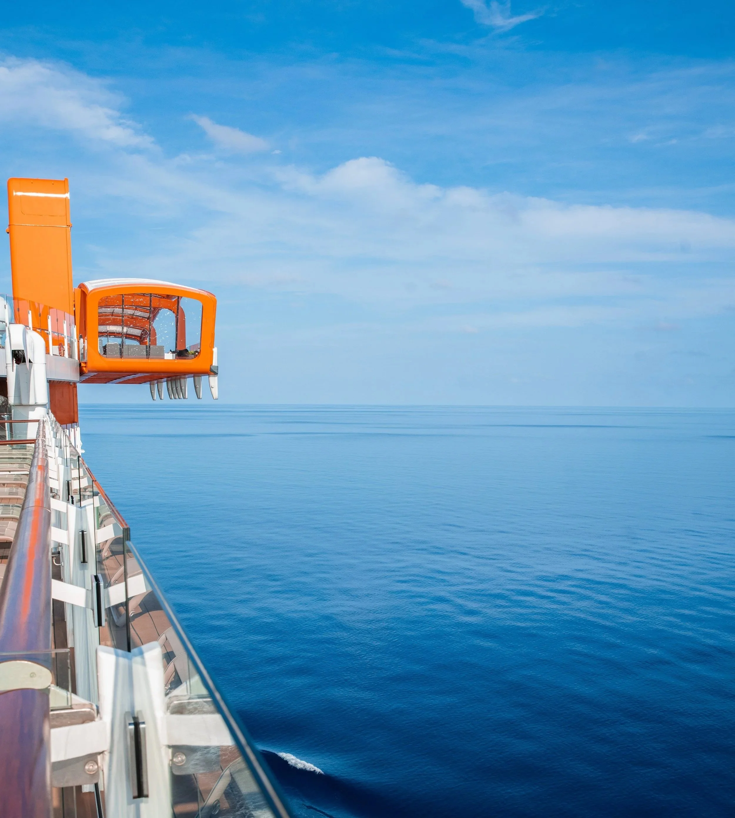 The Celebrity Cruises Magic Carpet, a bright orange cantilevered platform hanging over the side of an Edge-class ship, positioned over the ocean as an outdoor lounge.