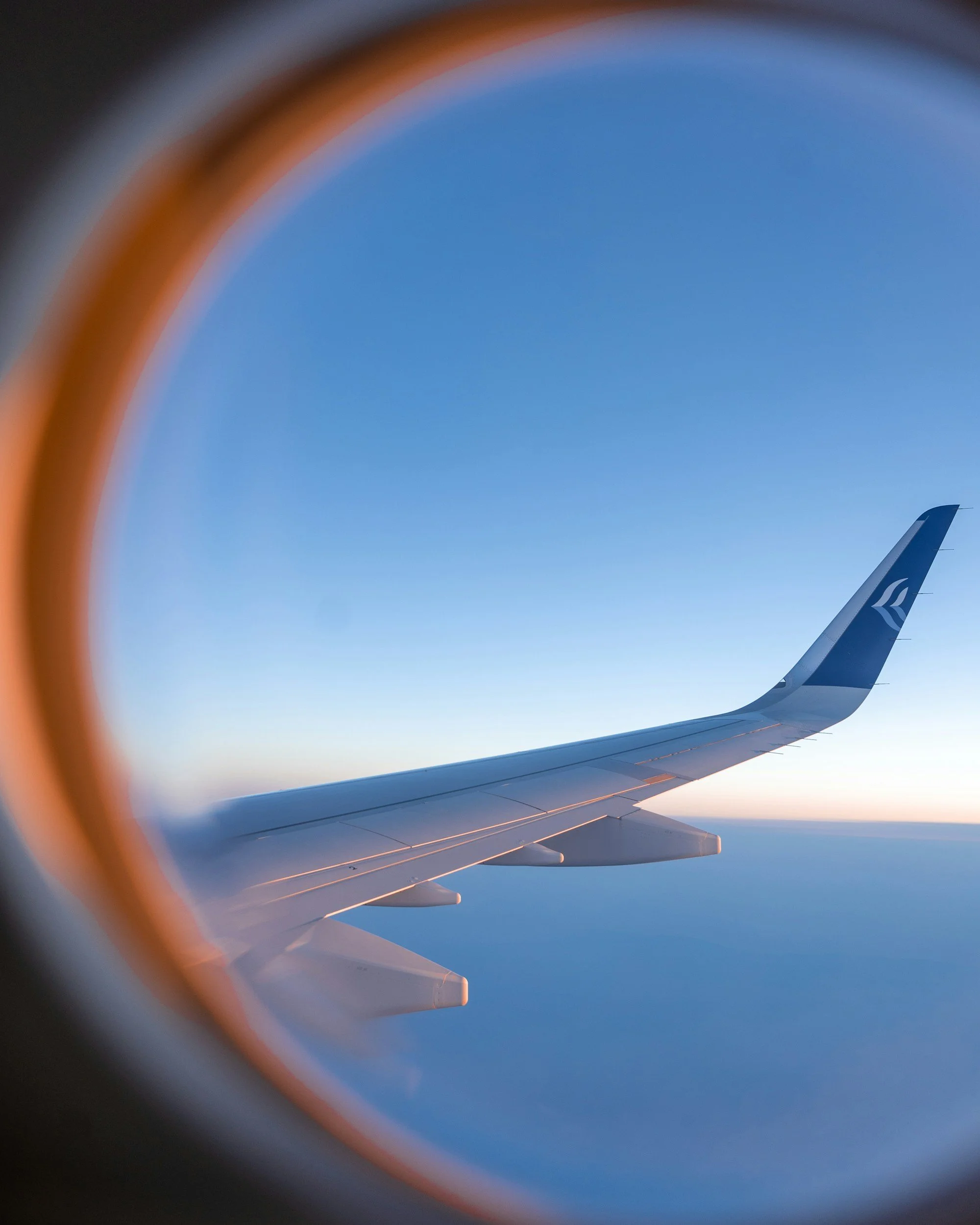 Airplane wing in flight over a scenic landscape, representing a seamless travel experience with Assured Travel.