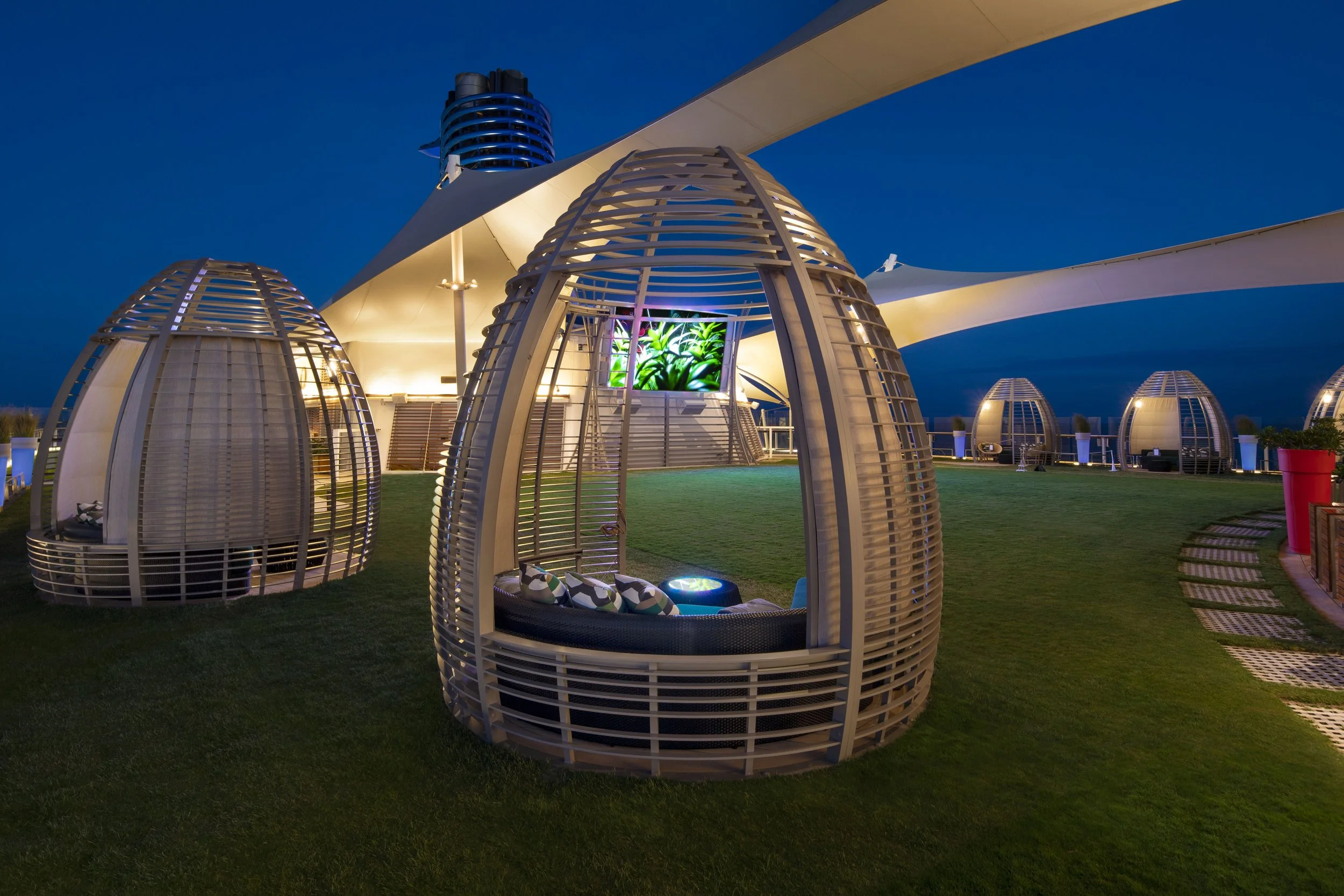 half-acre of real, manicured green grass on the top deck of a Celebrity Solstice-class ship, featuring Adirondack chairs and sunset views.
