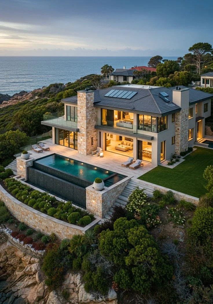 Maison moderne en bord de mer avec piscine extérieure et véranda, entourée de végétation, sous un ciel nuageux, vue sur l'océan.