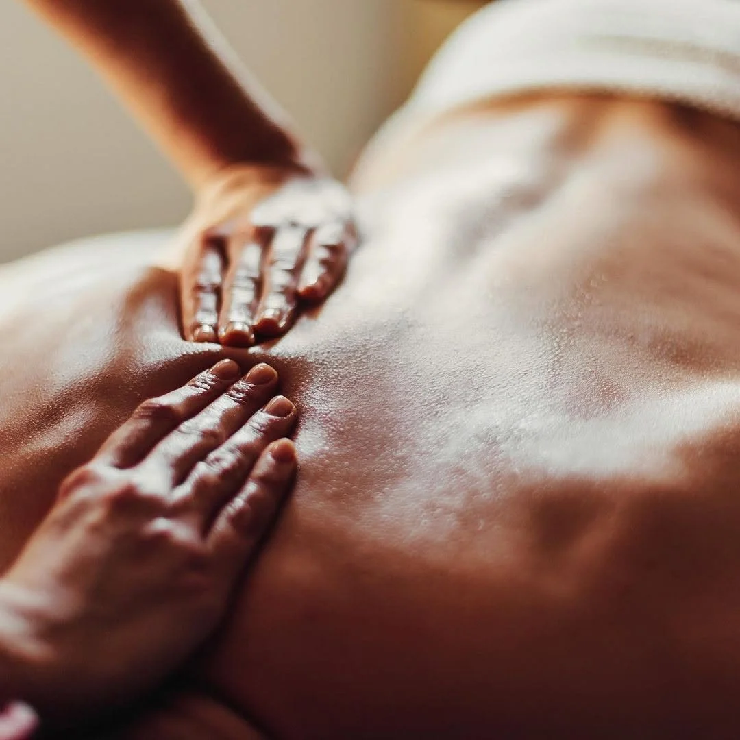 Une personne reçoit un massage sur le dos, avec de la crème ou de l'huile sur la peau.