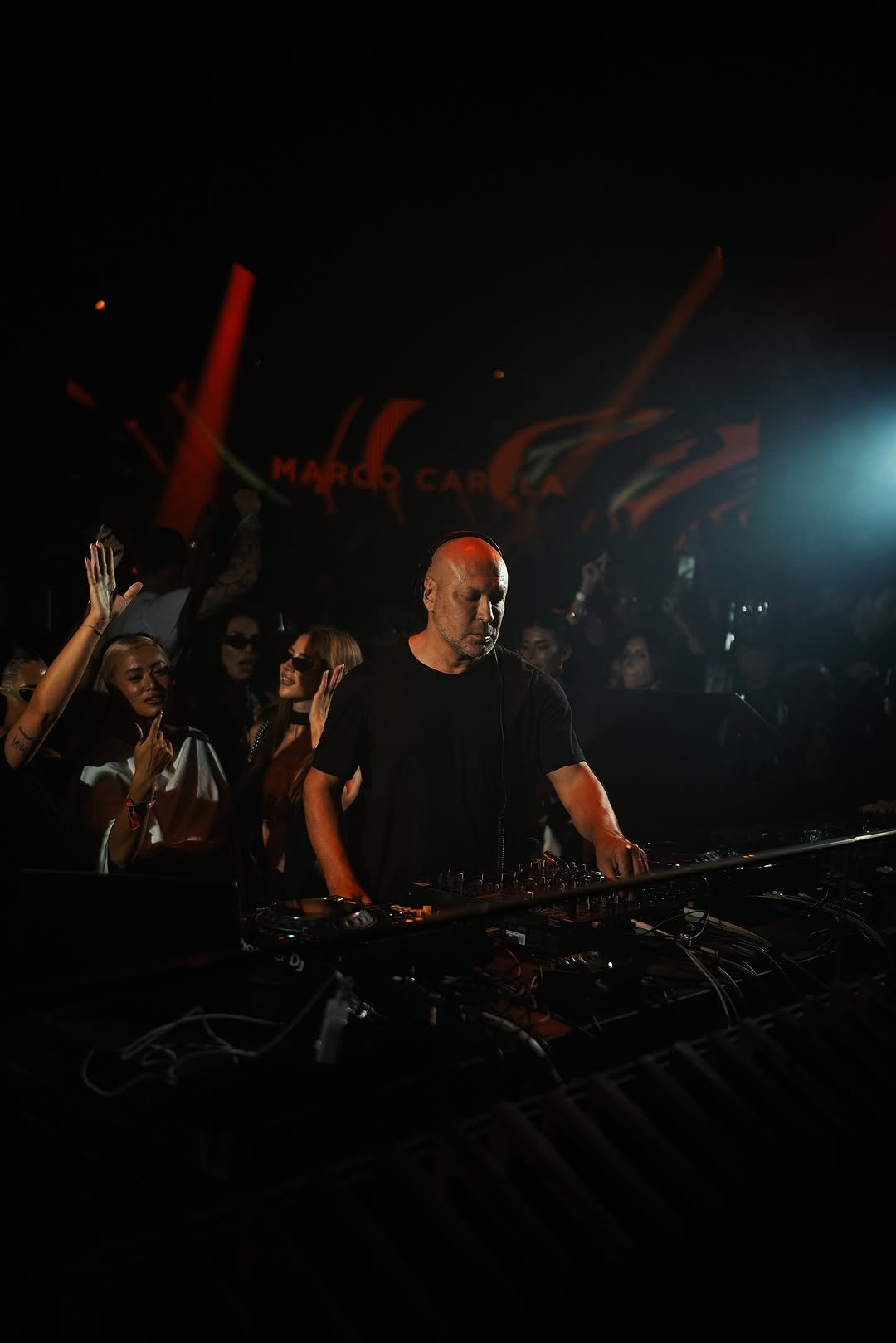 DJ en retrait sur scène avec un public enthousiaste, ambiance sombre avec éclairage coloré.