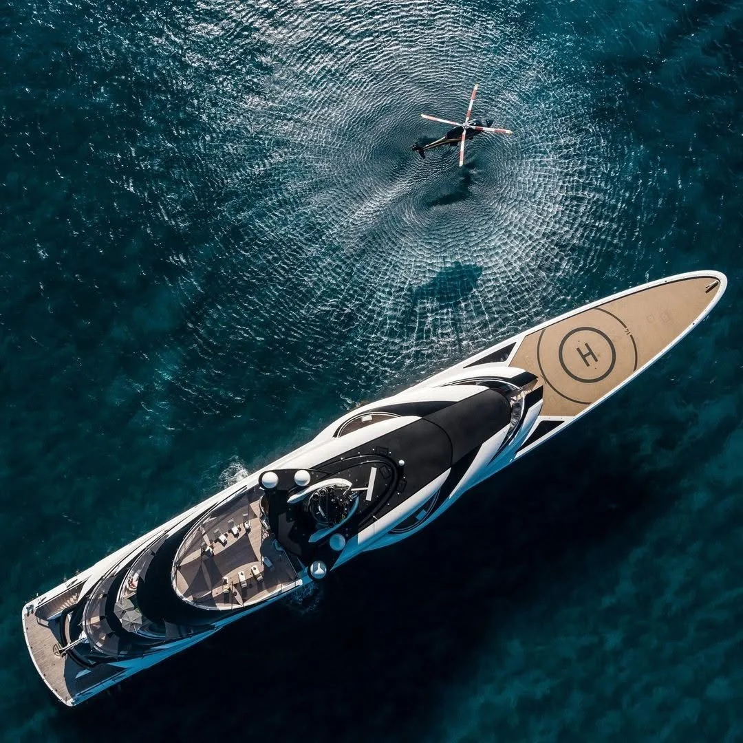 Vue aérienne d’un yacht de luxe avec héliport, naviguant sur une mer turquoise.