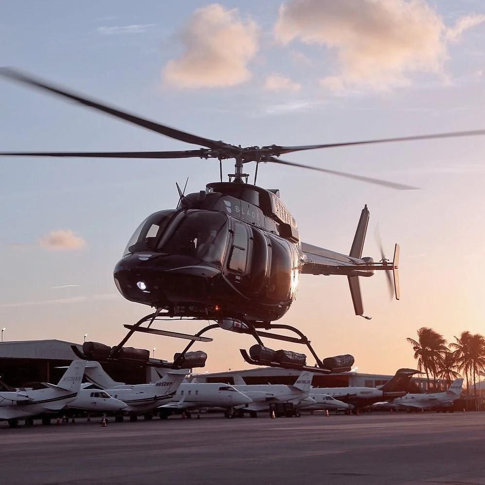 Un hélicoptère noir en vol stationnaire au-dessus d'un parking d'avions privées au coucher de soleil