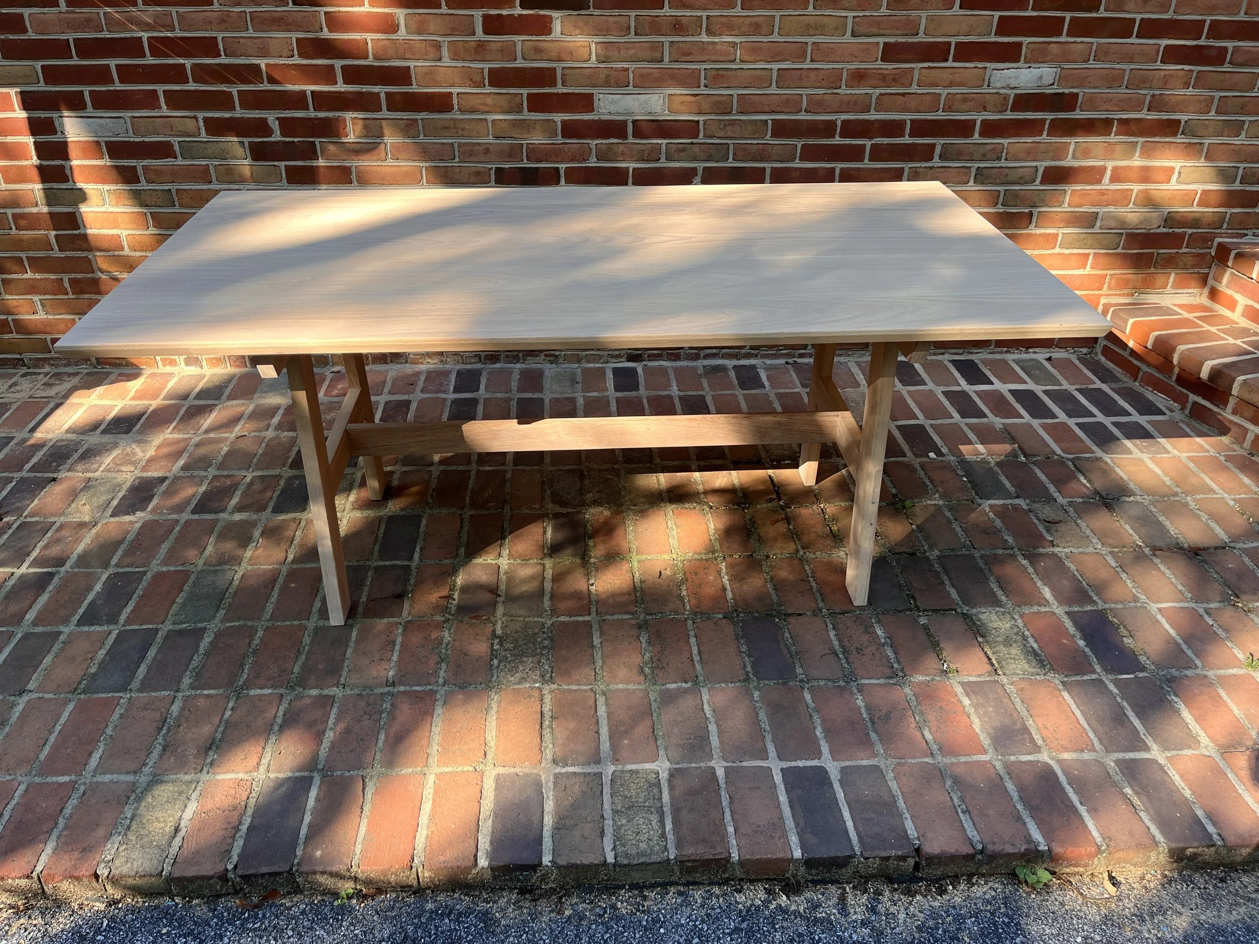 A wooden table on a brick patio, with shadows cast by nearby objects and a brick wall in the background.