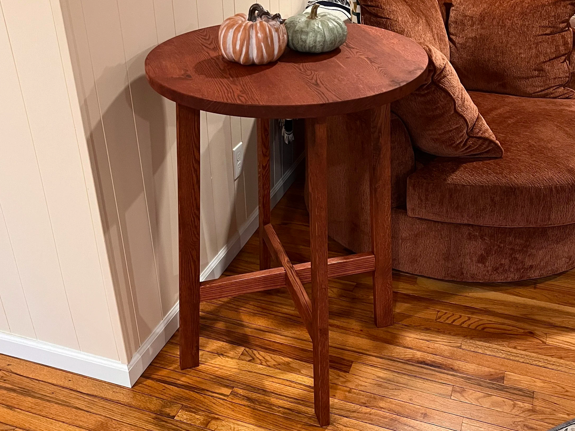 A small round wooden side table with decorative pumpkin-shaped items on top, situated next to a brown upholstered sofa.