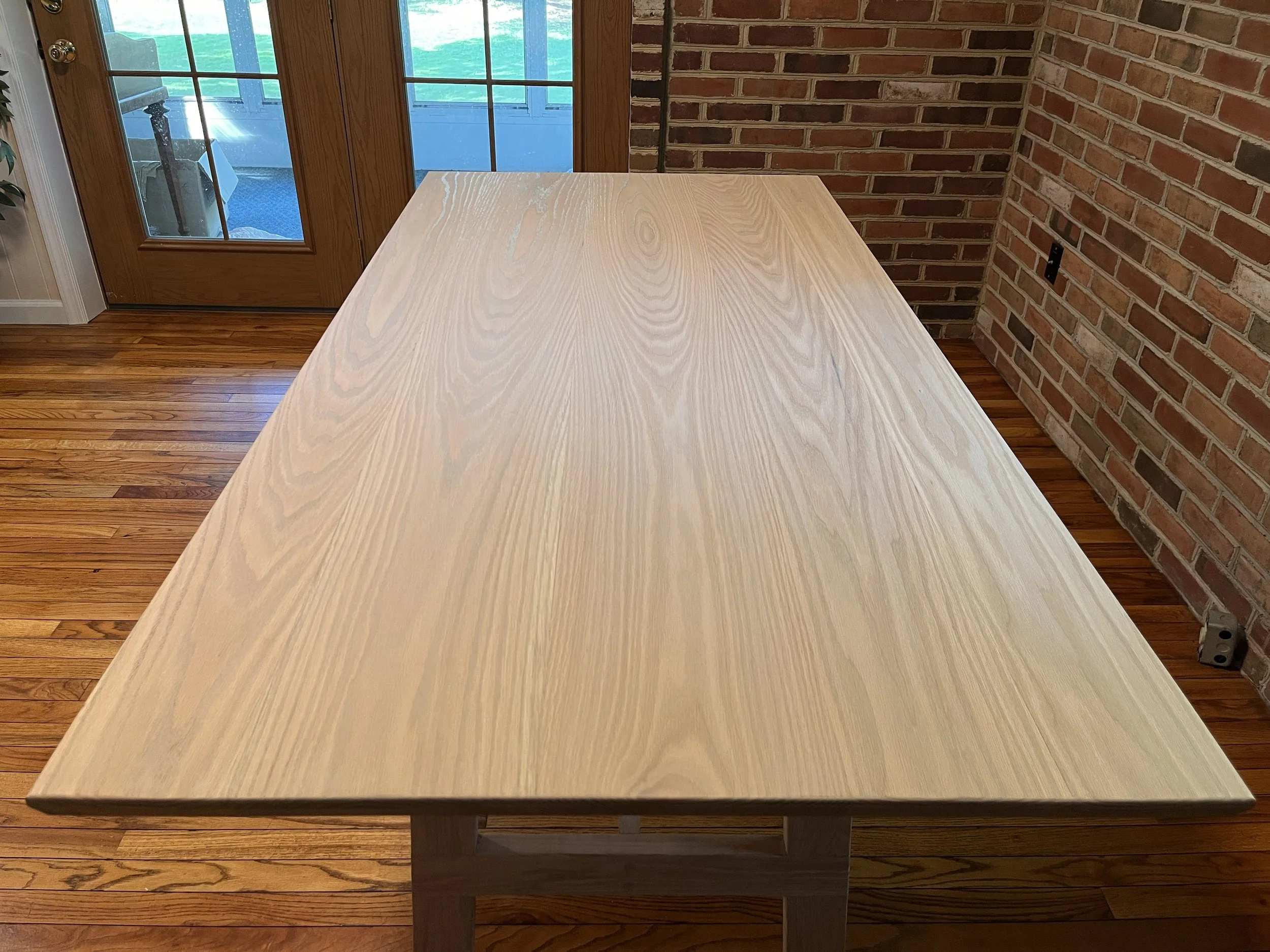 Empty wooden table in a room with a brick wall and glass doors leading outside.