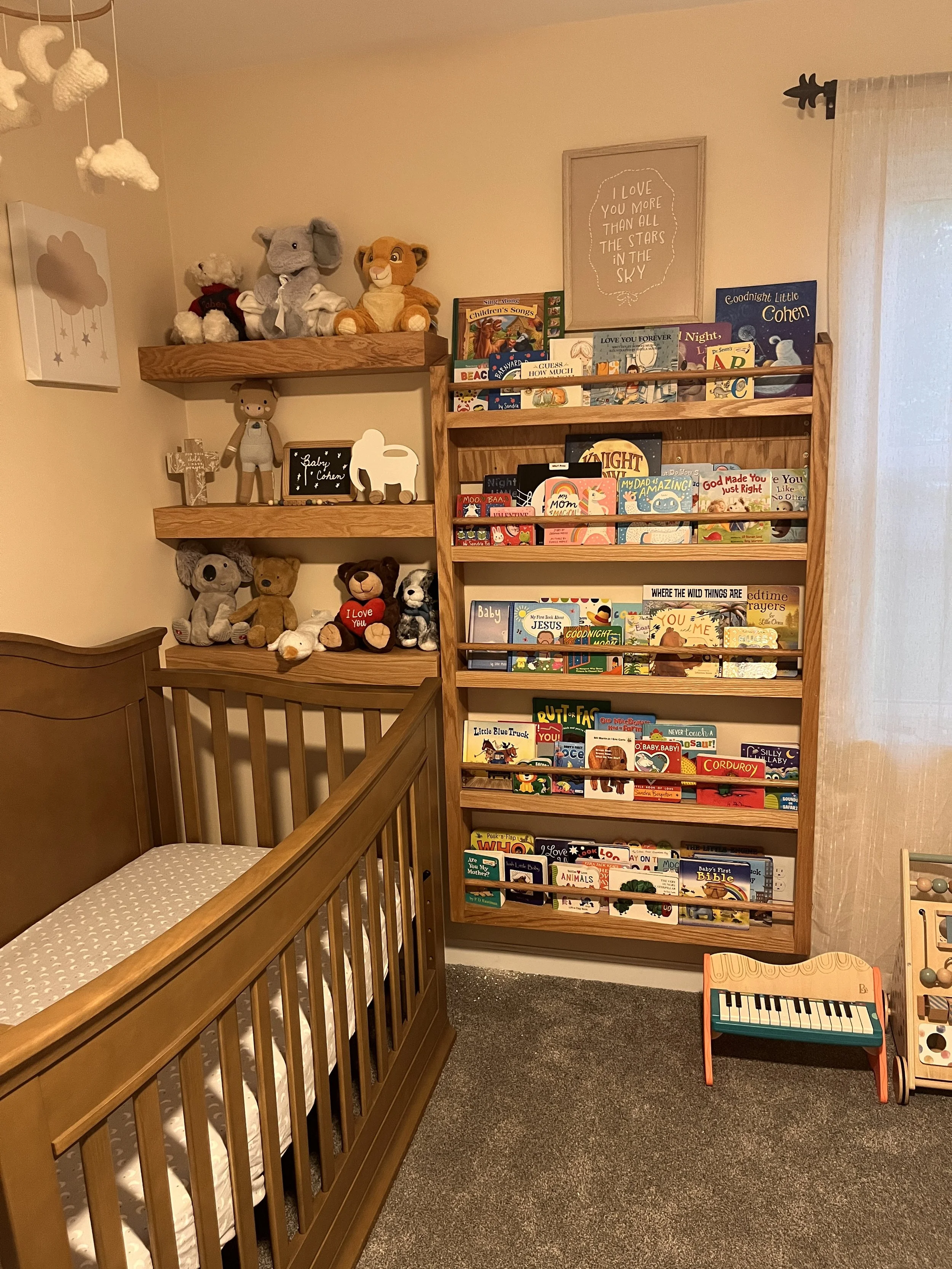 A nursery corner with a wooden crib, shelves filled with children's books, plush toys, decorated wall art, and a toy keyboard.