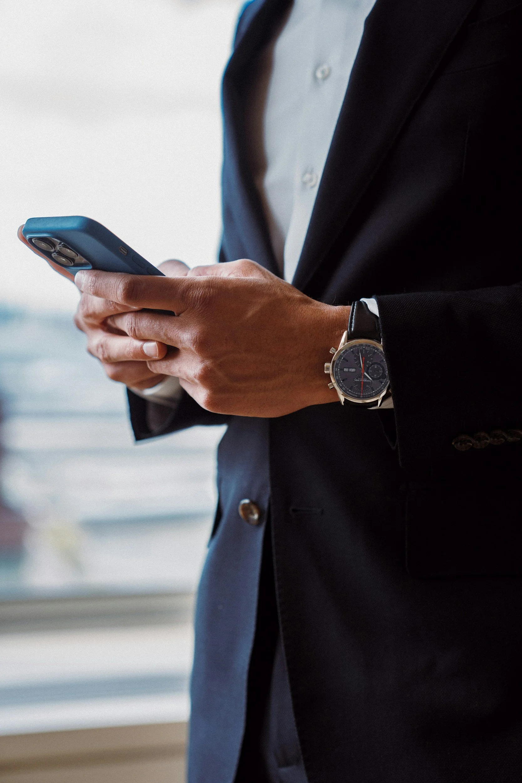 A man in a business suit using a smartphone with a city view in the background.