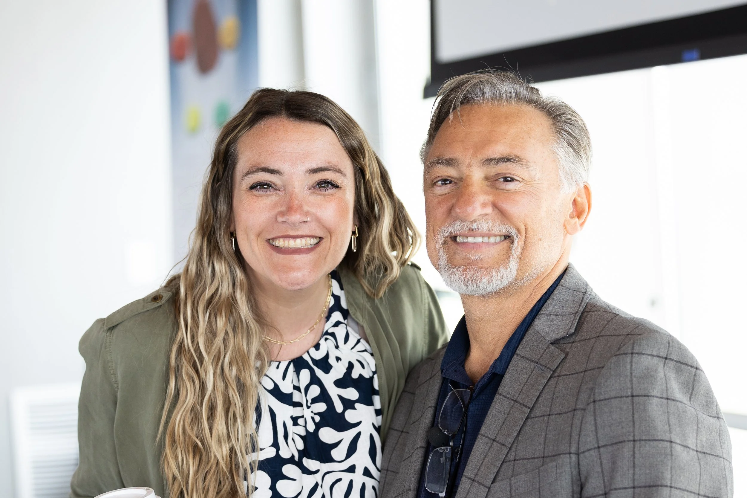 Smiling woman and man in professional attire taking a selfie in an office setting.