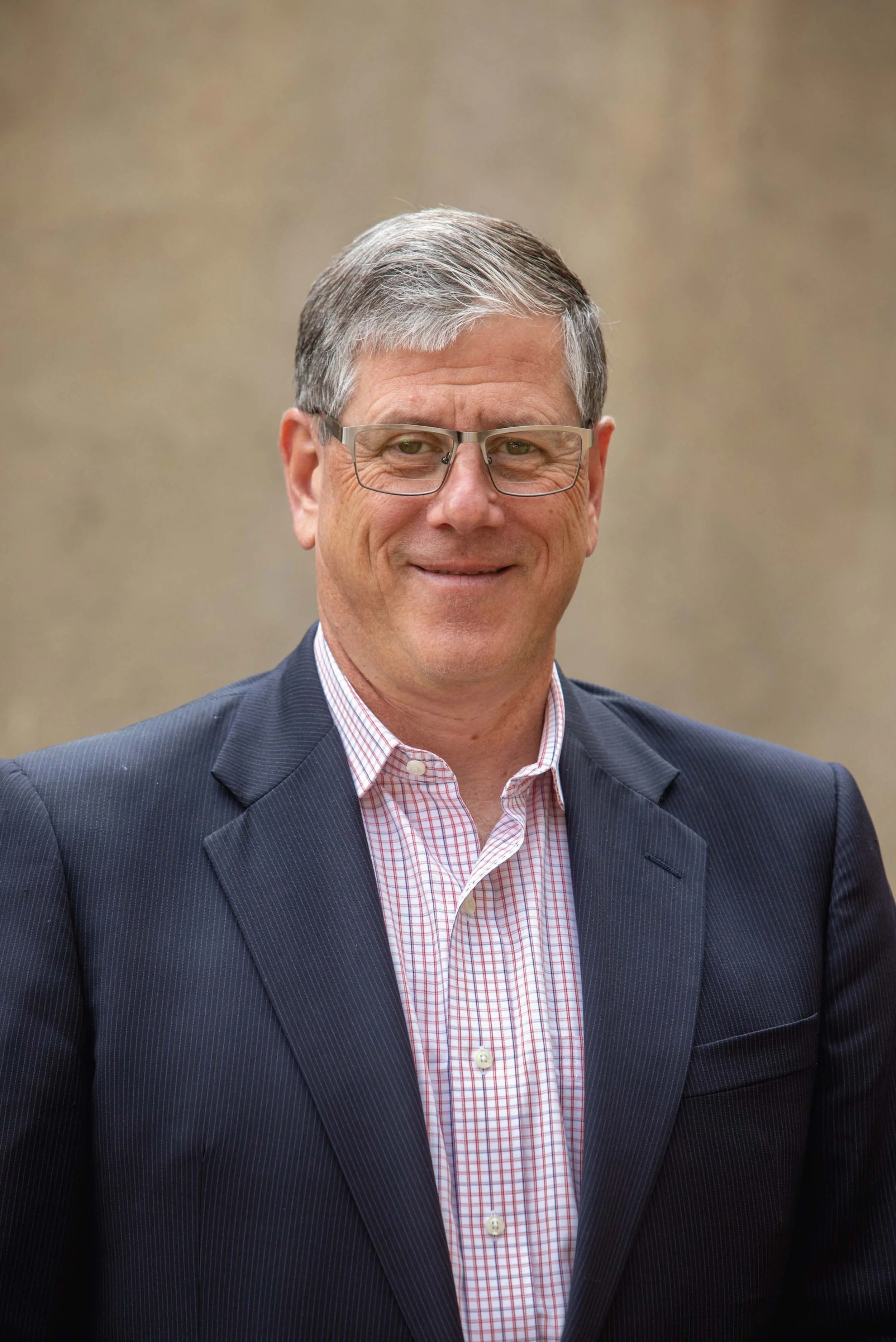 A smiling middle-aged man with gray hair wearing gray blazer wearing glasses