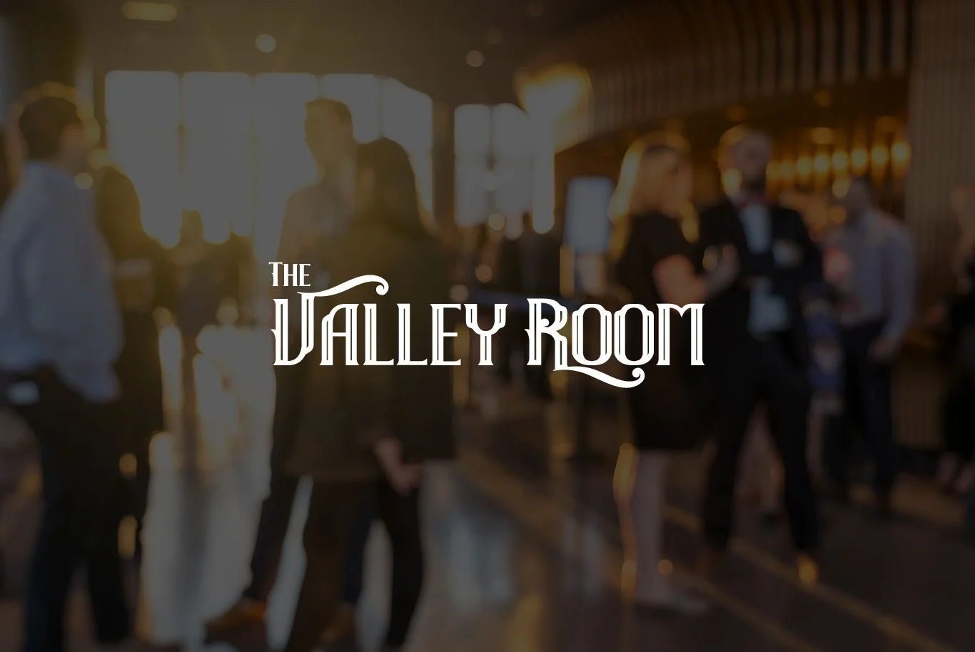 Blurred image of people in formal attire socializing in a warmly lit lounge area with wooden accents, overlaid with the text "The Valley Room".