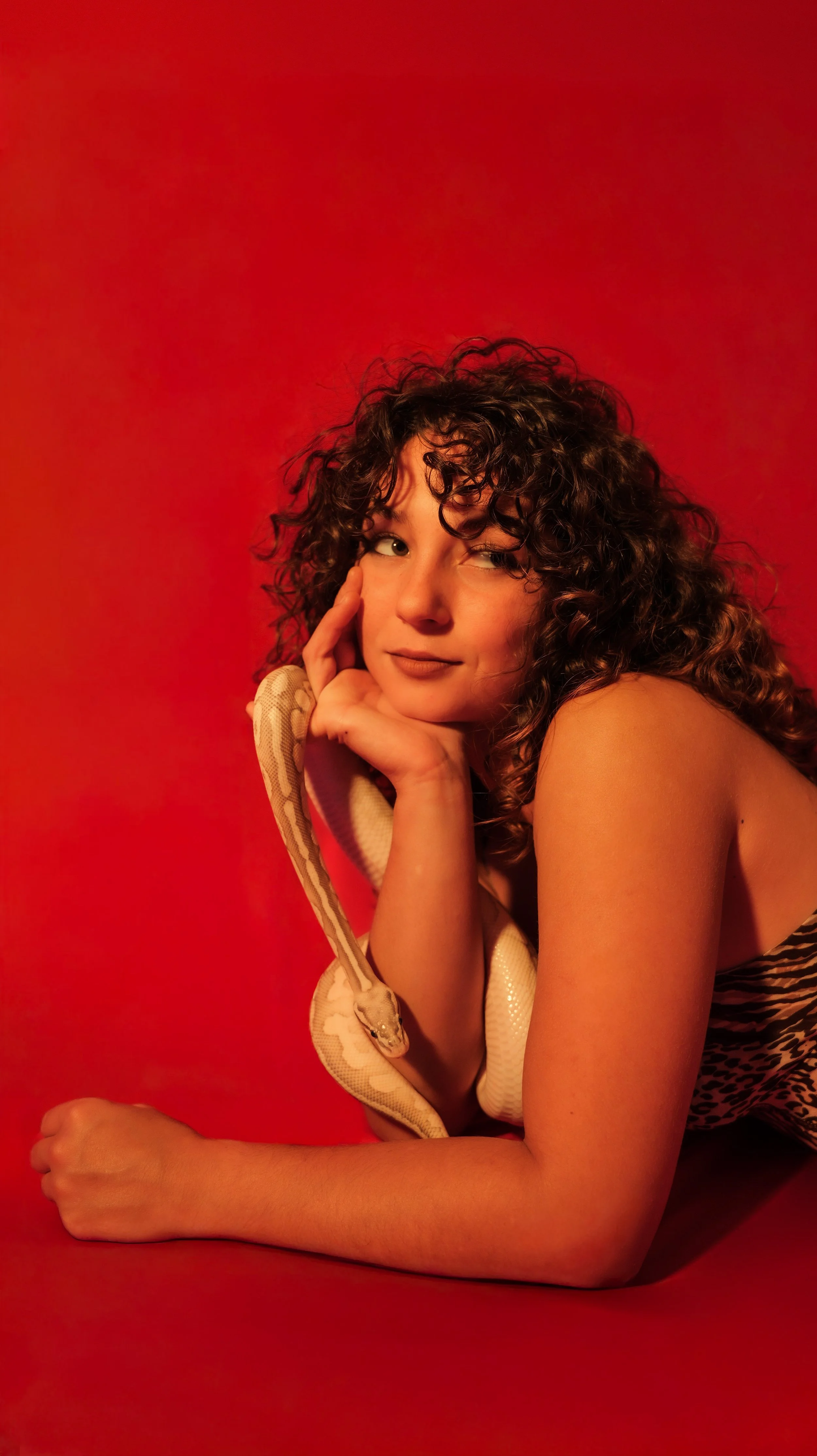 Young woman with curly hair posing with a snake on a red background.