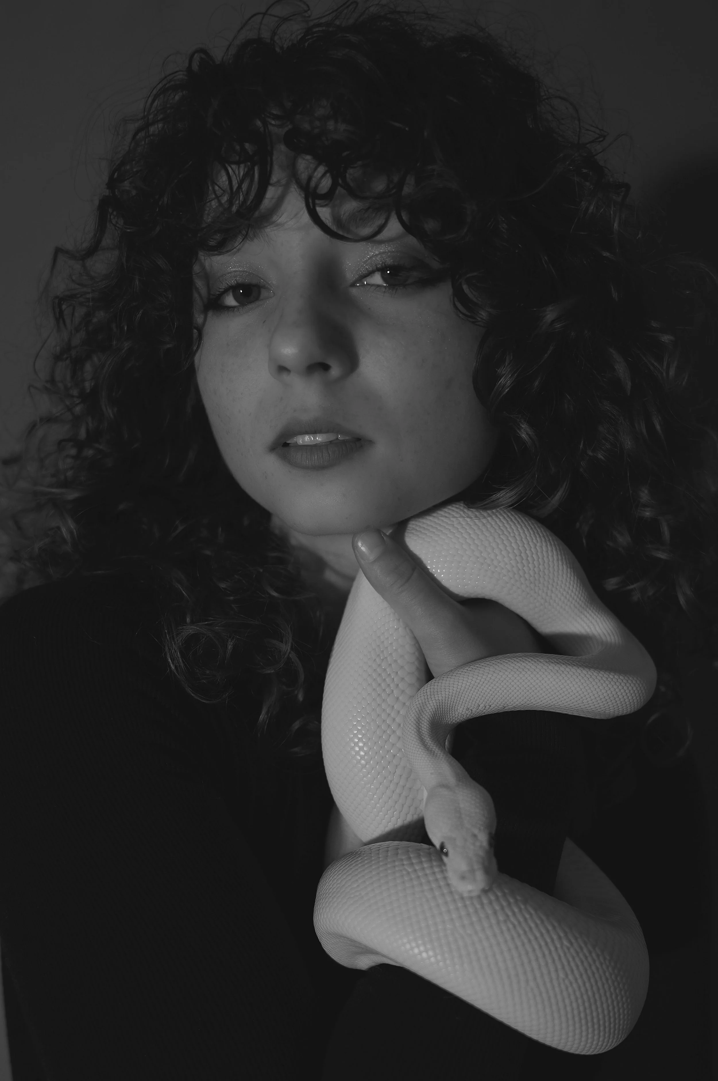 Black and white photo of a woman with curly hair holding a white snake, with direct gaze and slightly parted lips.