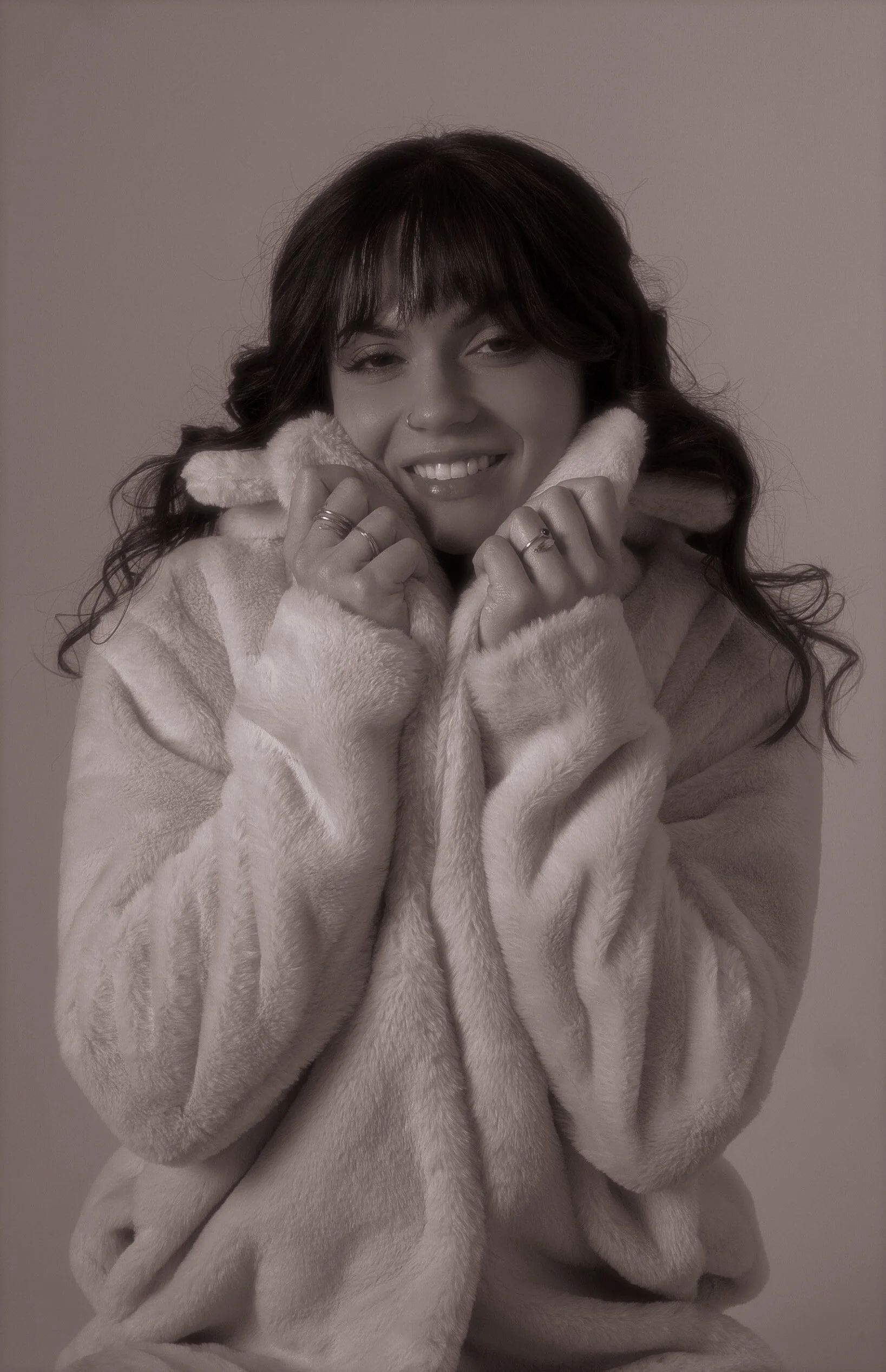 A woman smiling, wearing a cozy, fuzzy coat and holding the collar close to her face.