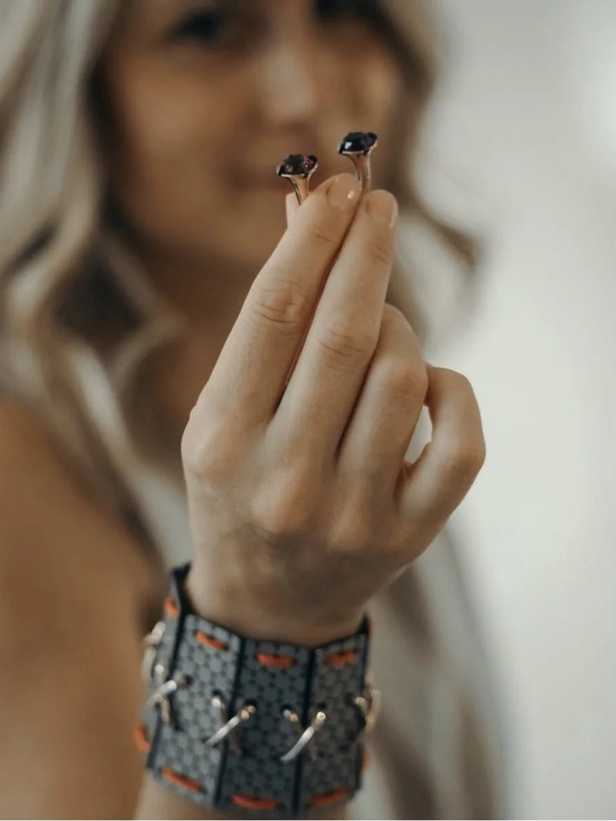 A woman holding two small black objects with pink and white details between her fingers, with her face blurred in the background.