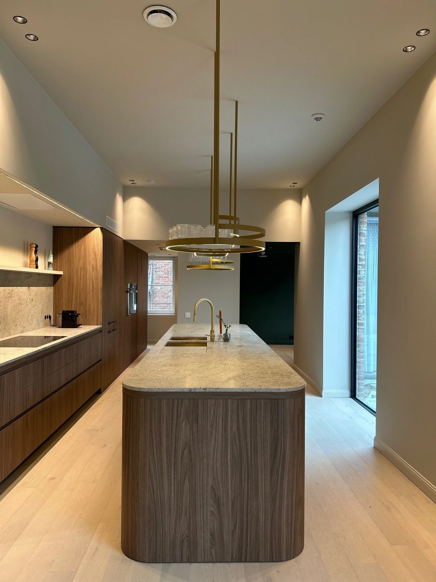 Modern kitchen with a large wooden island and marble countertop, pendant lighting fixtures, built-in appliances, and a sliding glass door leading outside.