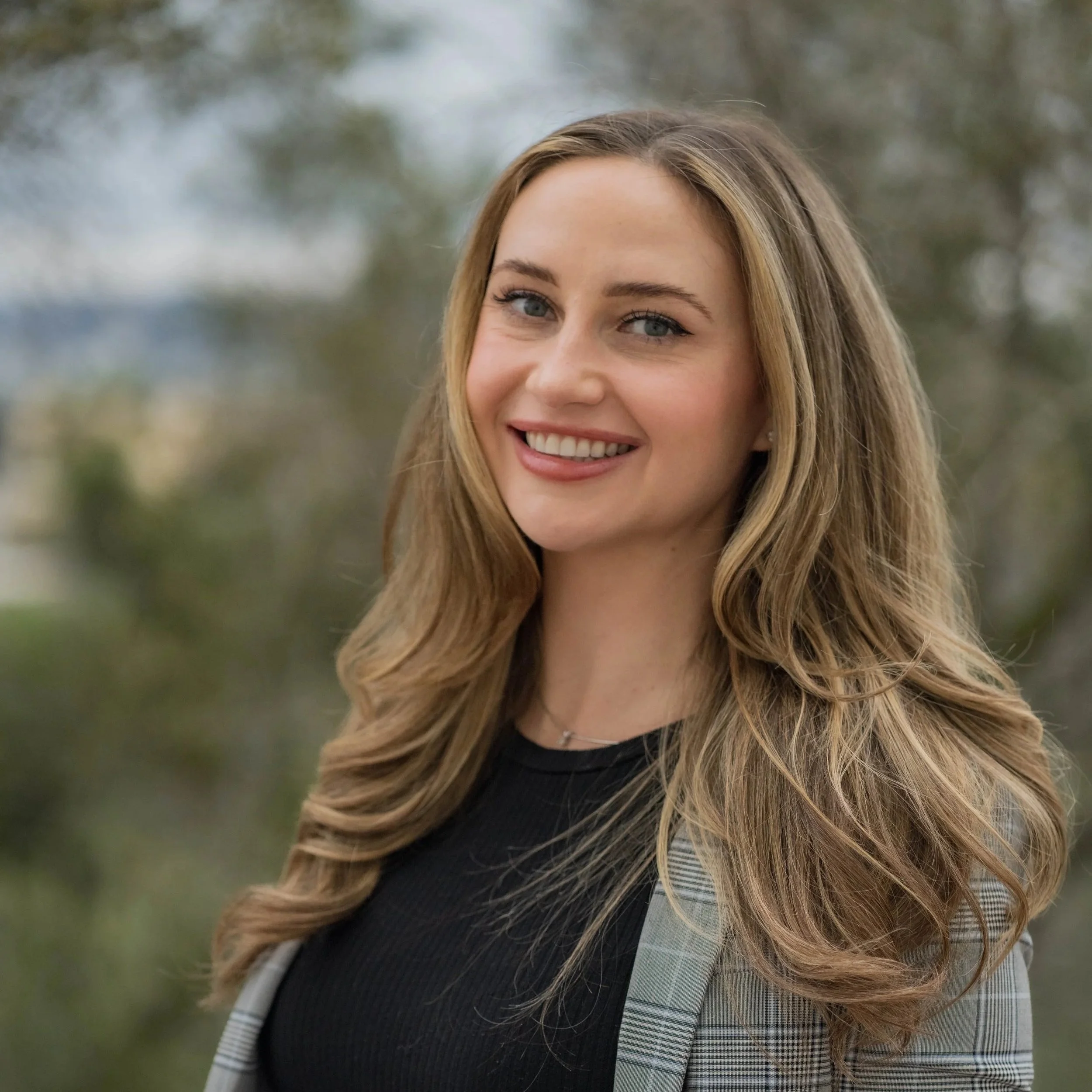 Your Therapist: A young woman with long wavy blonde hair, smiling outdoors with a blurred natural background.