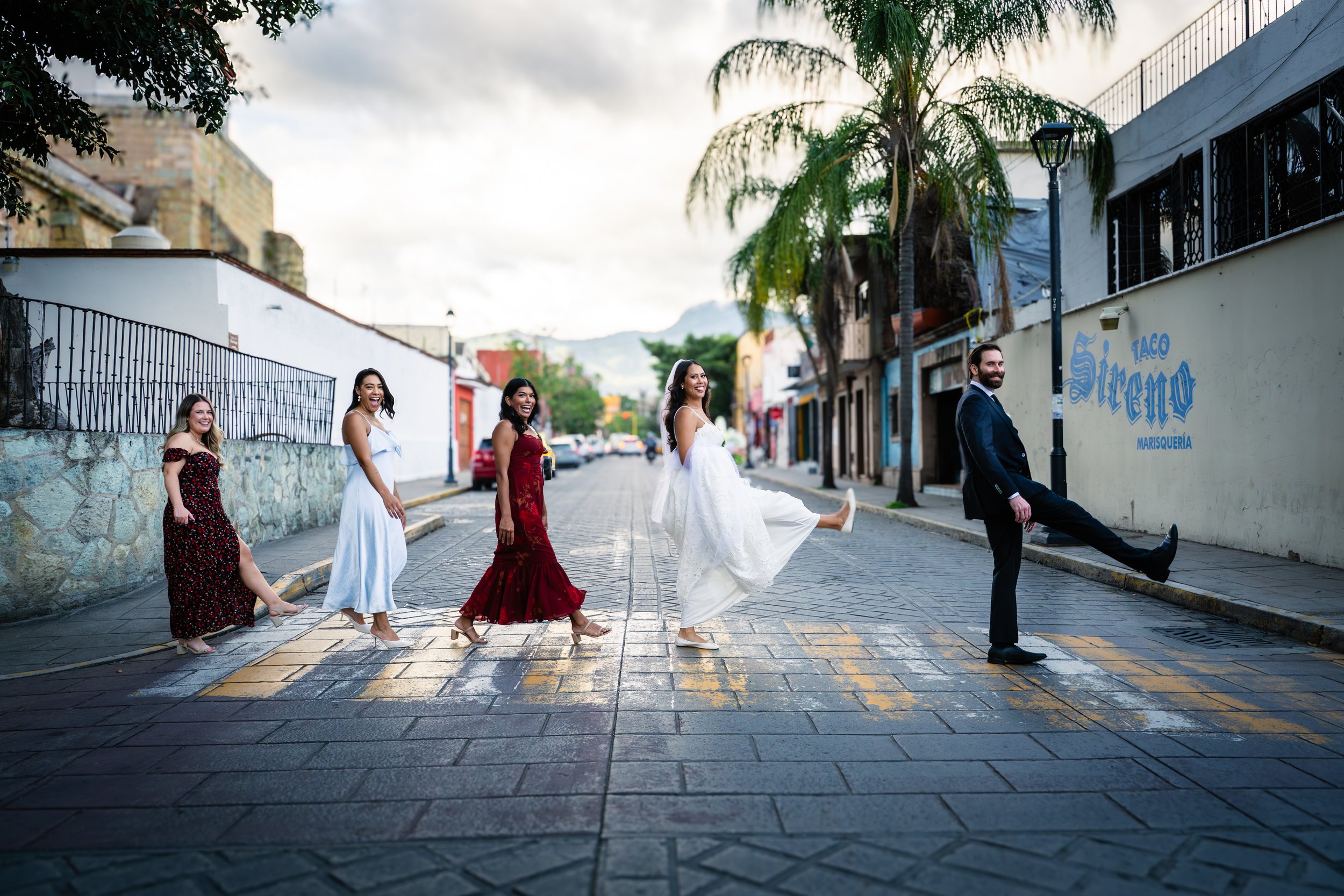 Maried couple in the middle of Oaxacan street with people walking like the Beatles in a pathway. Oaxacan wedding.