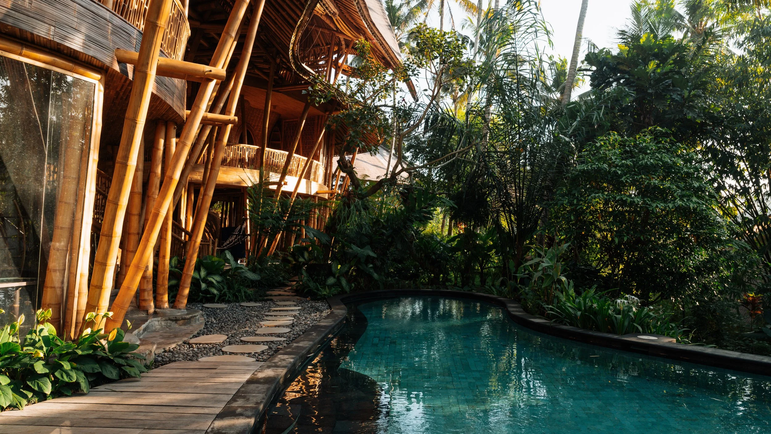 Villa Kelapa at sunset — bamboo architecture and turquoise pool, Green Village, Bali. Luxury villa photography in golden light.