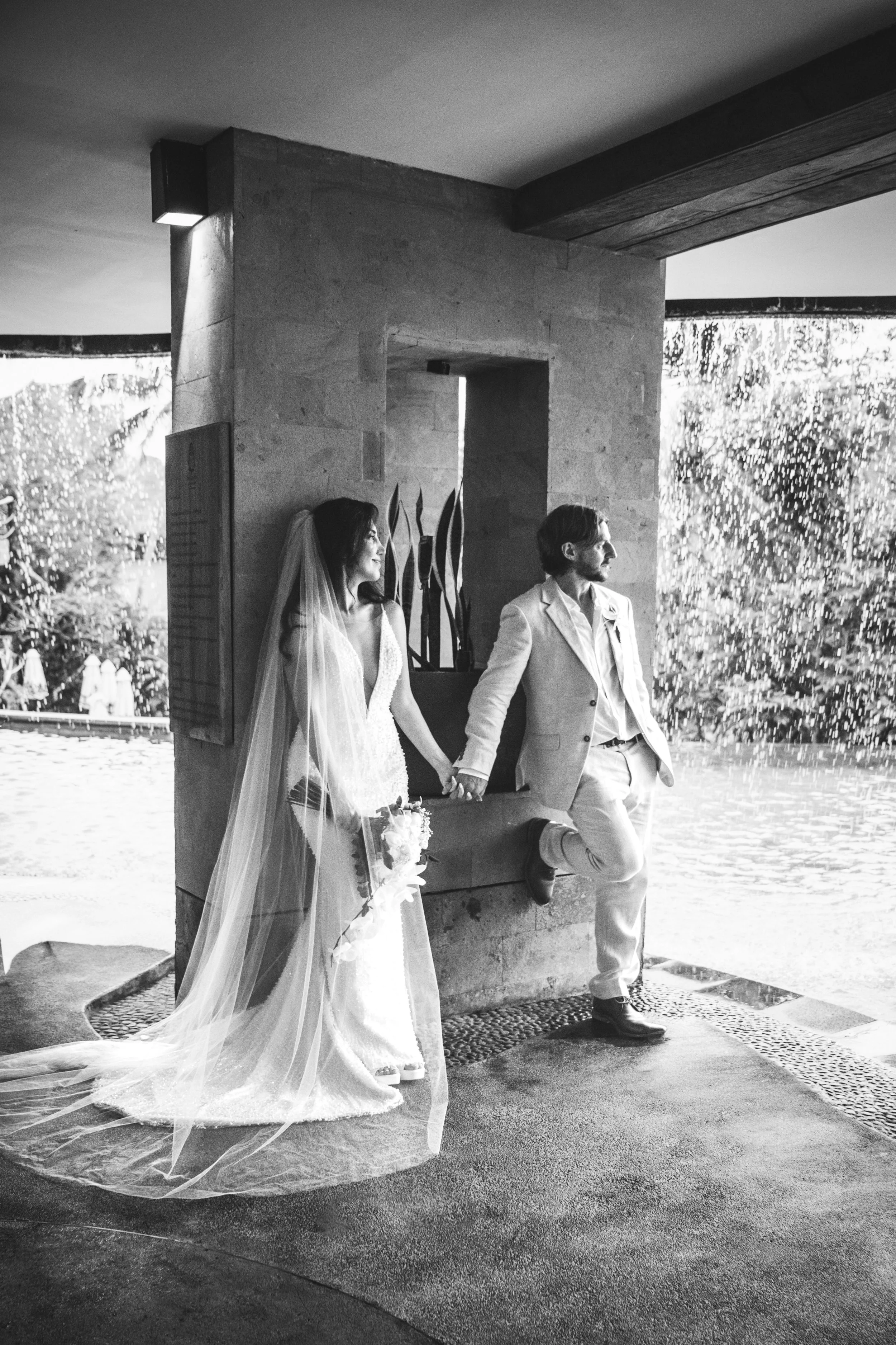 Rainy Bali wedding photography — bride and groom embracing in the rain, jungle canopy and Kanyon Ubud villa in the background, a spontaneous romantic moment.
