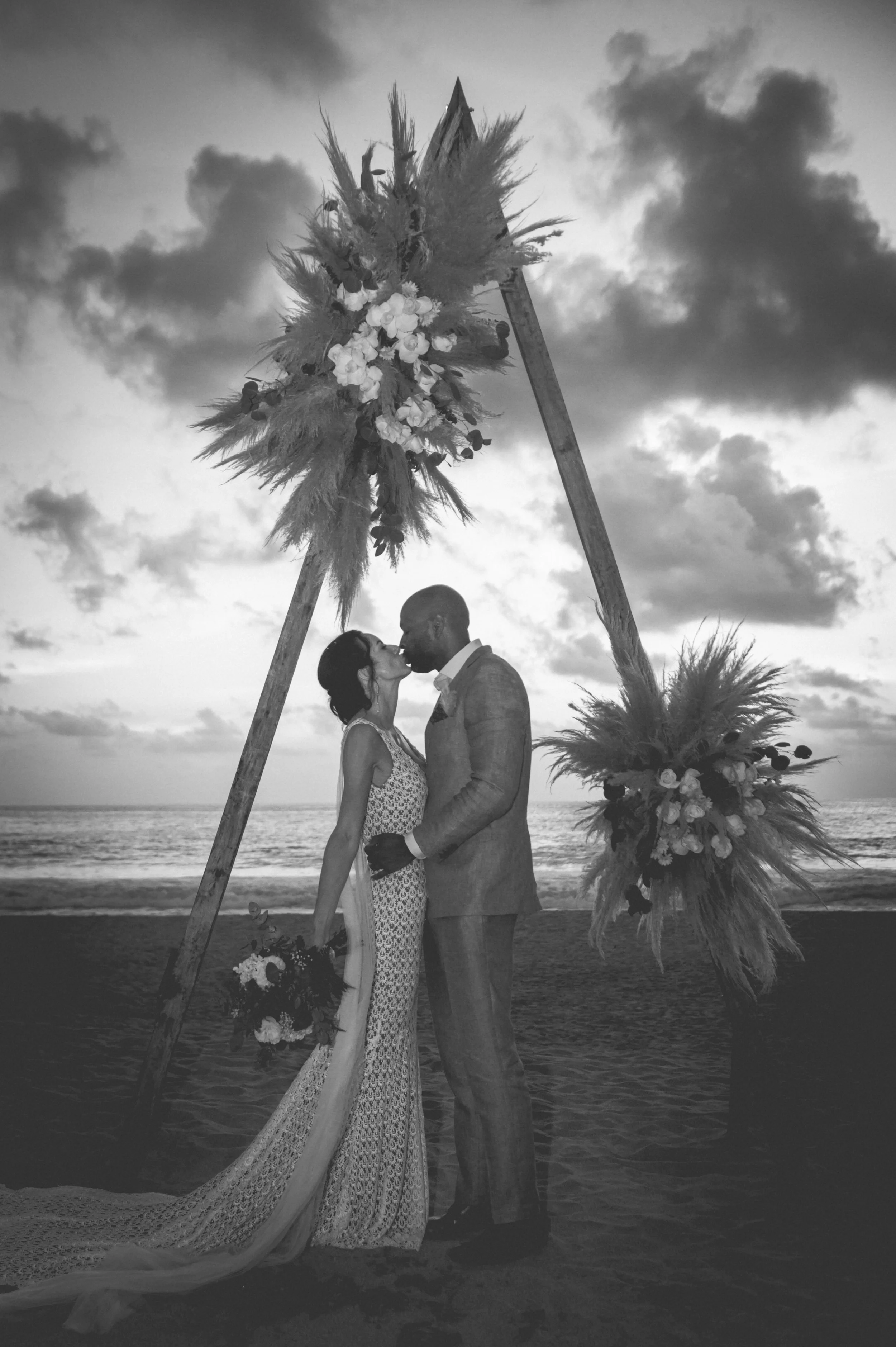 Wedding ceremony in Puerto Escondido where an american couple from San Francisco are kissing in front a beautiful sunset at the beach in Puerto Escondido. Amazing frame and luxurious wedding dress. black and white photography.