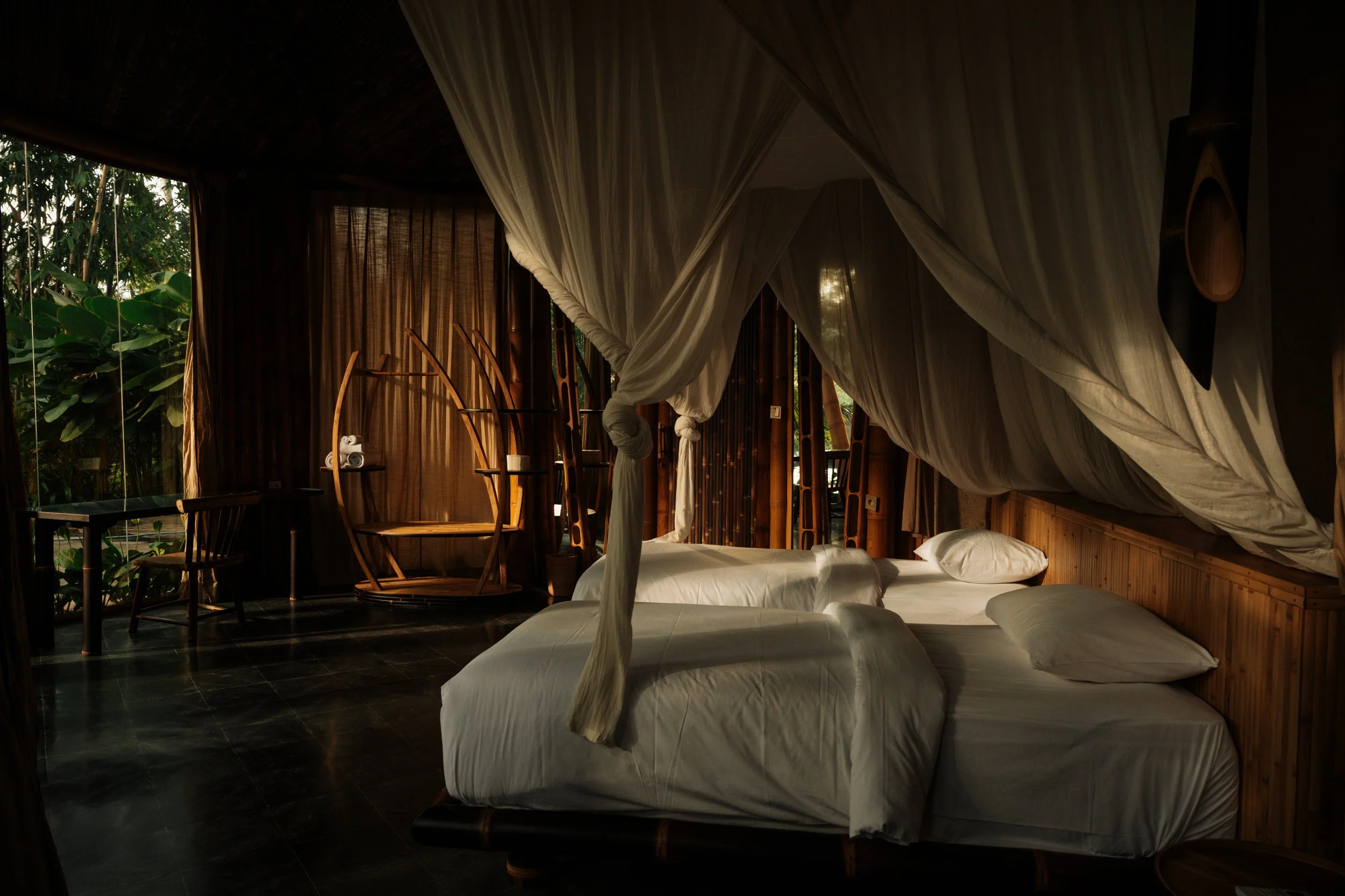 Bedroom opening onto the jungle, Villa Kelapa Green Village. Linen canopy beds, bamboo architecture, full tropical immersion.
