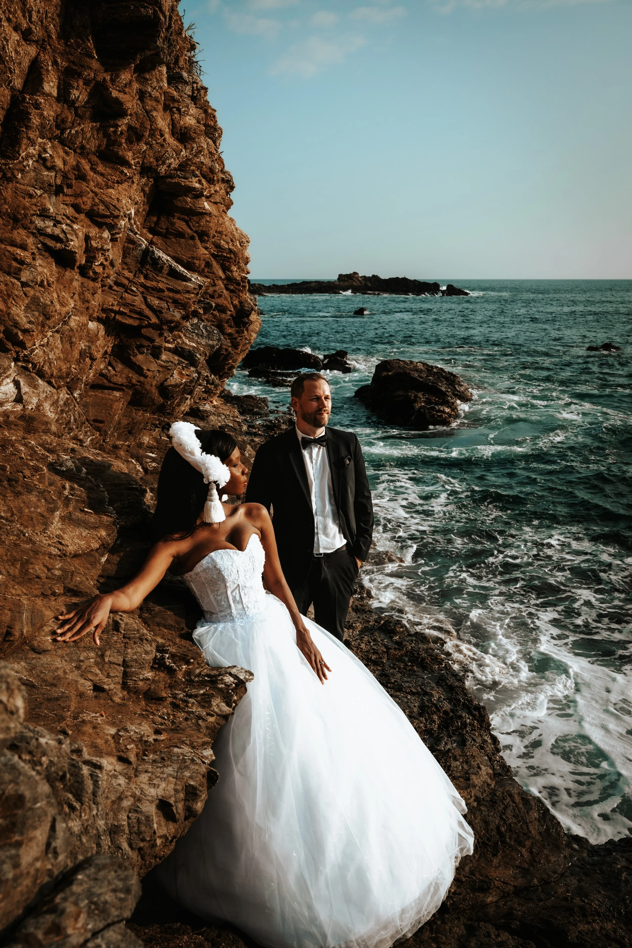 Editorial destination wedding photography in Oaxaca, featuring a couple seated on coastal rocks, looking toward the ocean in an atmosphere of refined intimacy.